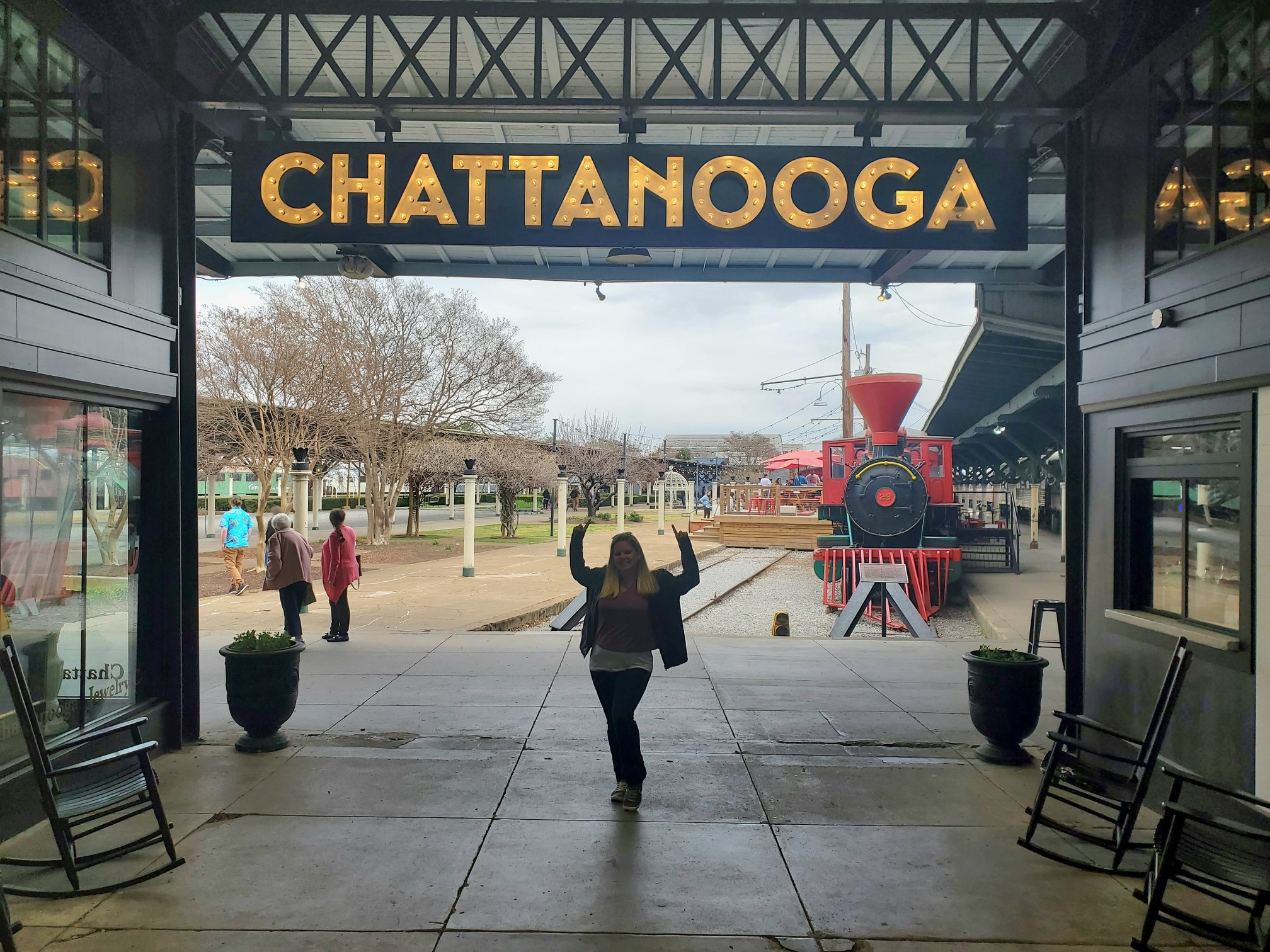 The image shows an entrance with the word “CHATTANOOGA” overhead, a person posing with arms raised and a red locomotive in the background.