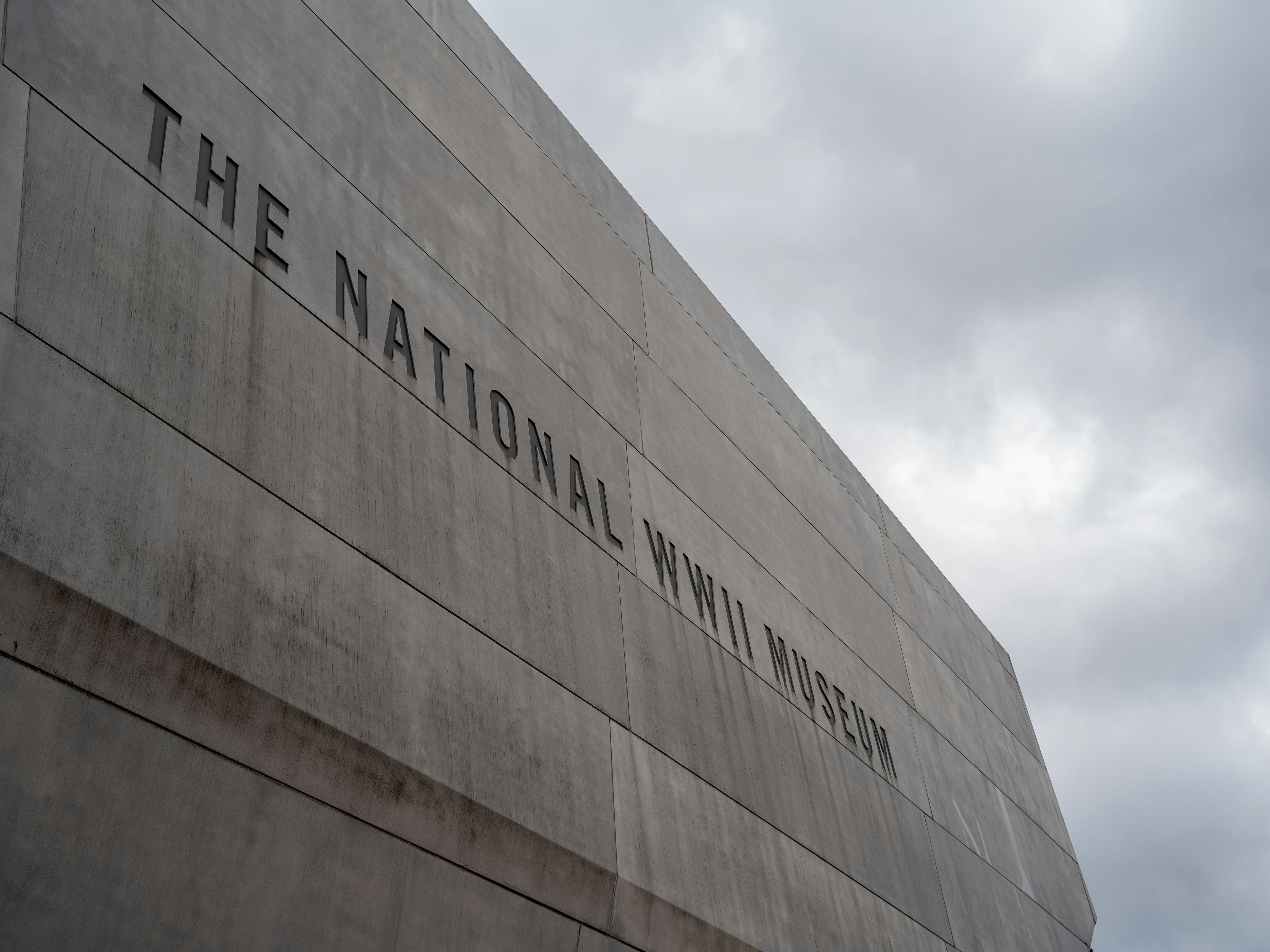 The facade of a building with “THE NATIONAL WWII MUSEUM” inscribed under a cloudy sky.