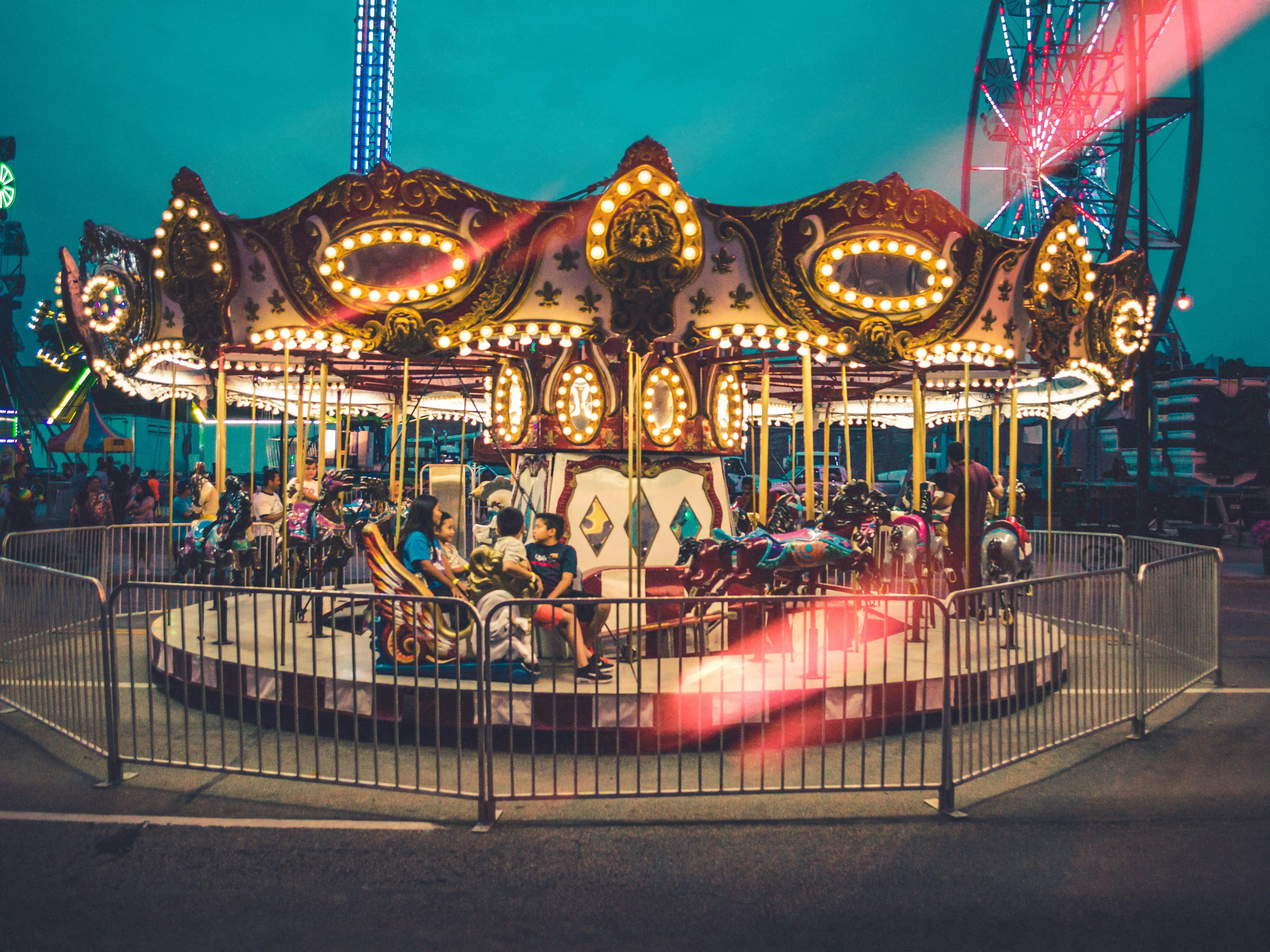 A carousel spins brightly at dusk, with a Ferris wheel in the background.