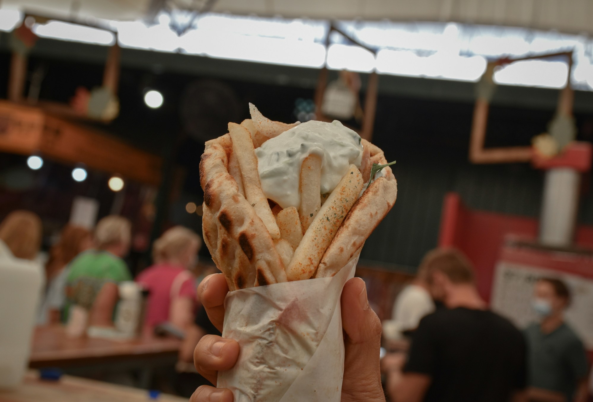 Person holding a wrap in their hand and a crowded restaurant behind them.