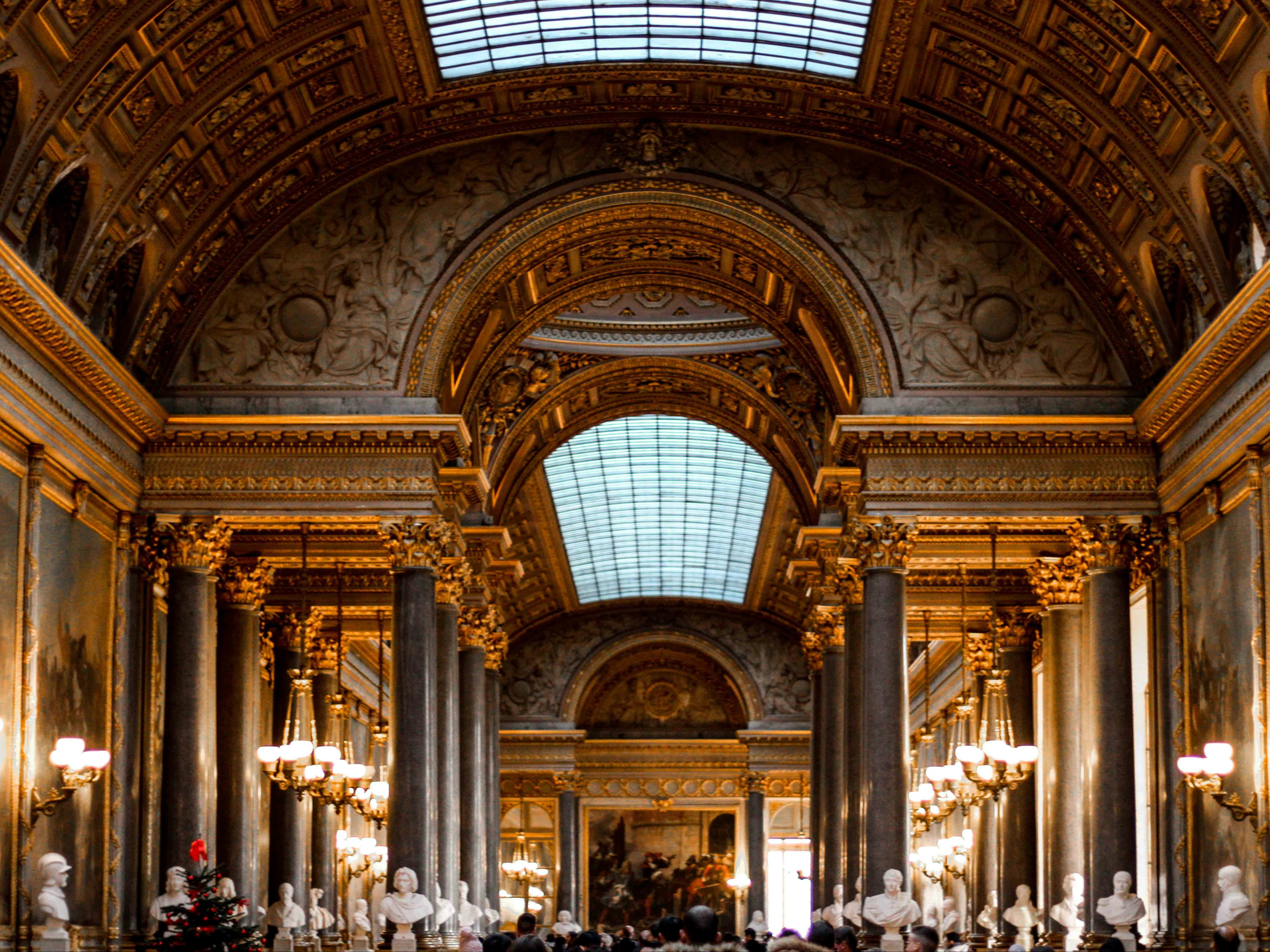 The image shows the interior of a grand, ornately decorated hall with arched ceilings, sculptures and chandeliers, suggesting a place of historical or cultural significance.