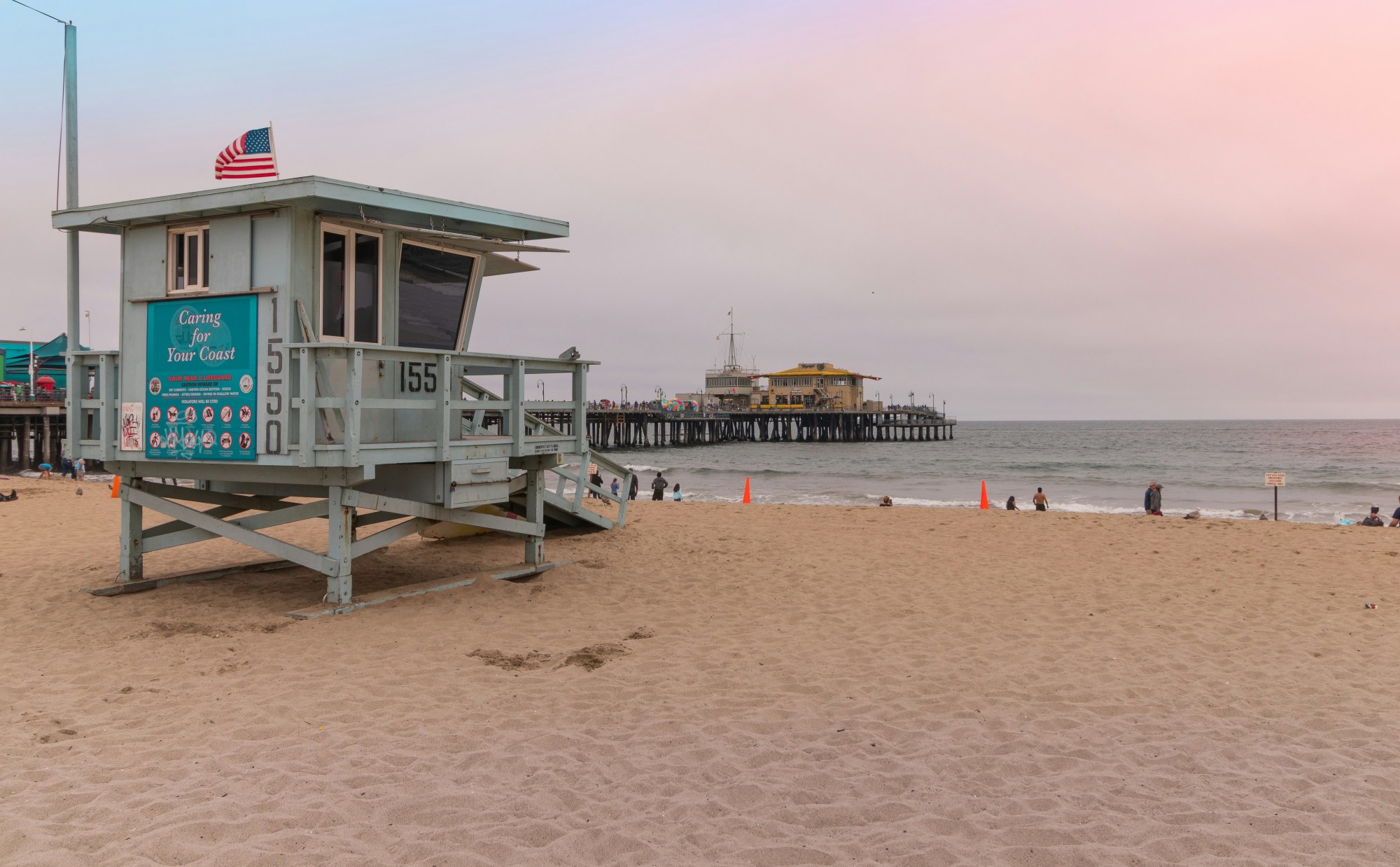 The Santa Monica pier reaches toward the horizon on a cloudy day as dusk.