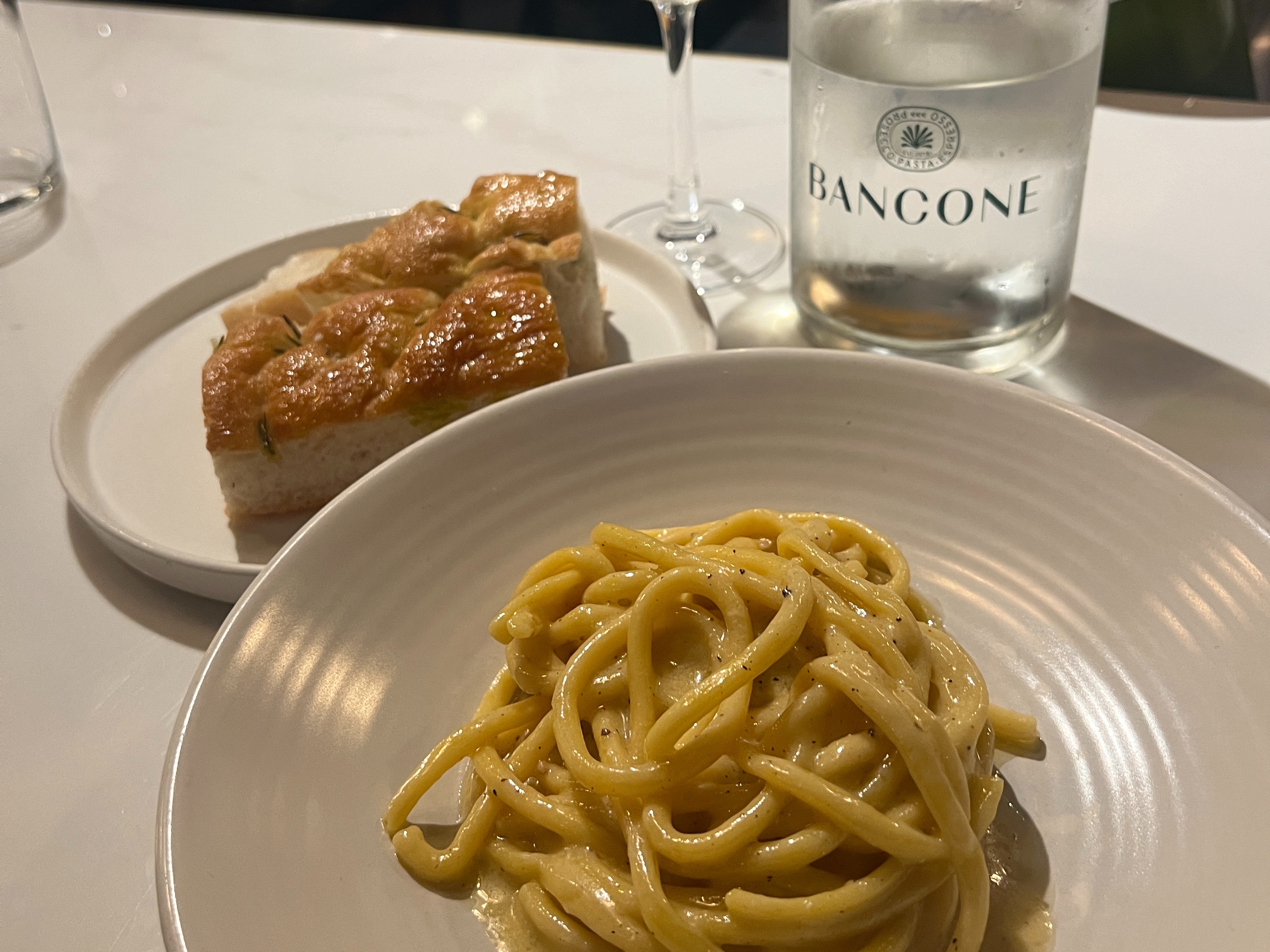 A plate of pasta next to a glass bottle of water