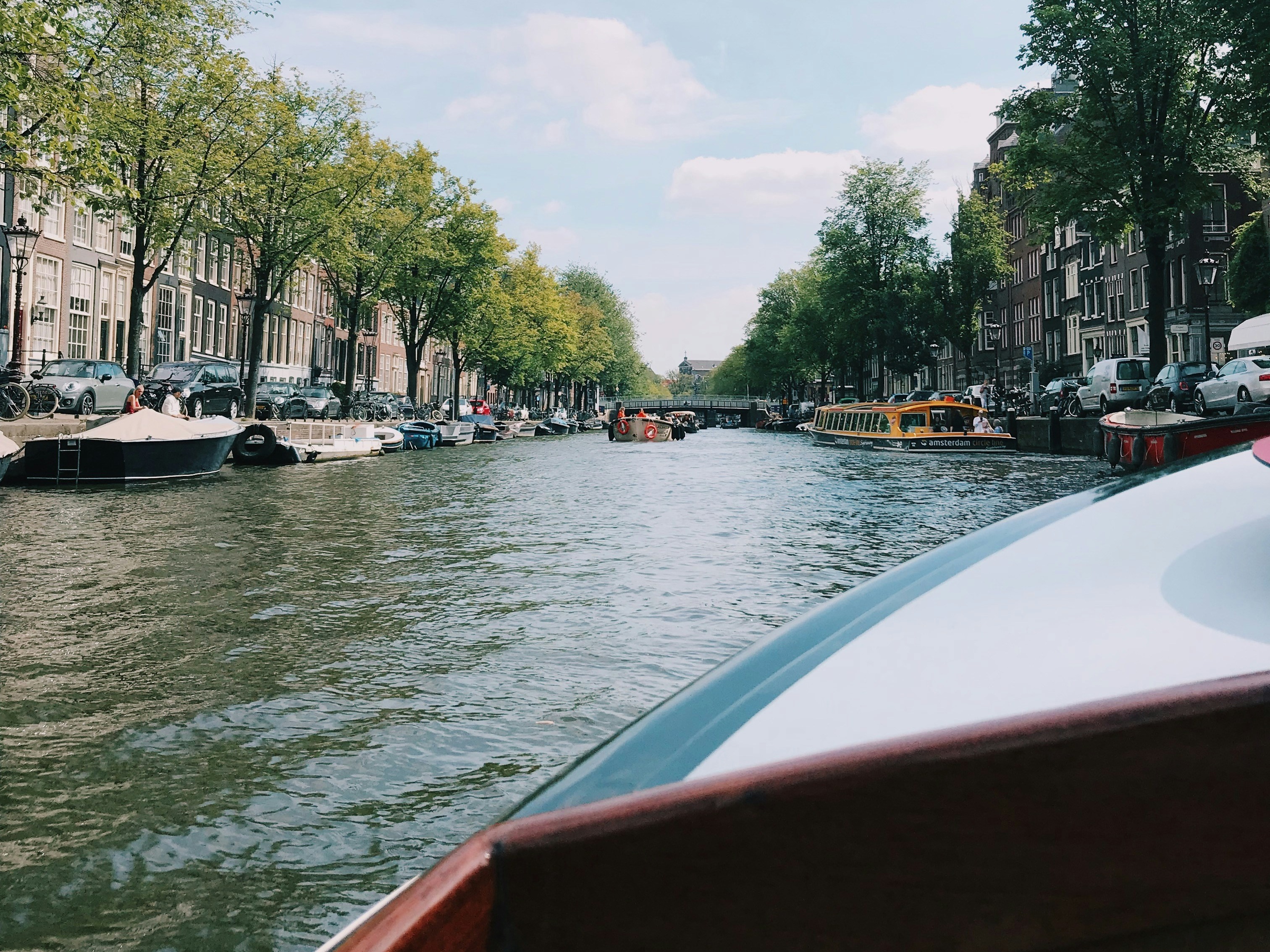 A view from a boat on a canal, lined with trees and historic buildings under a clear blue sky.