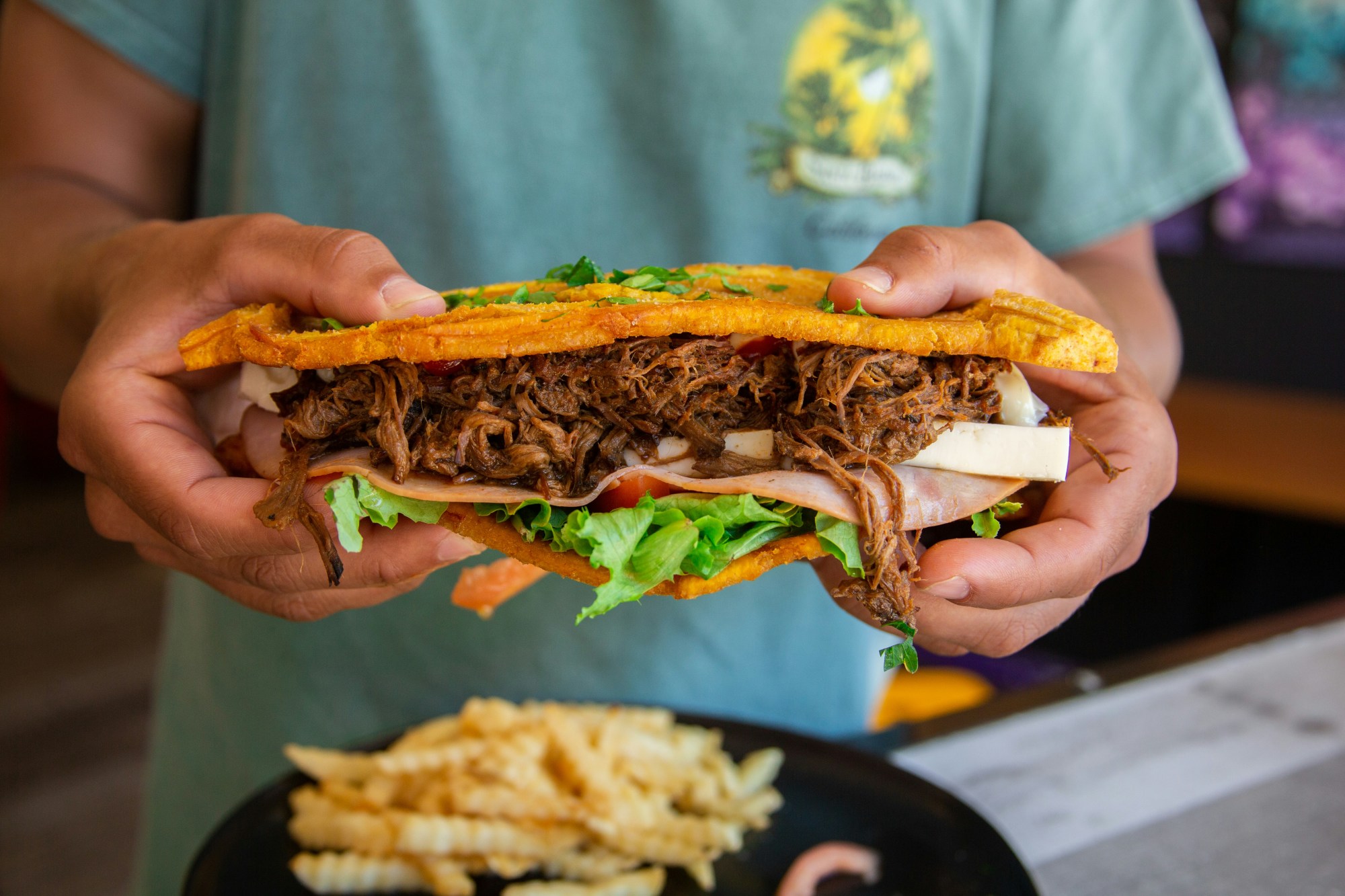 Server holding a giant overloaded sandwich stuffed with meats and veggies on a sunny day.