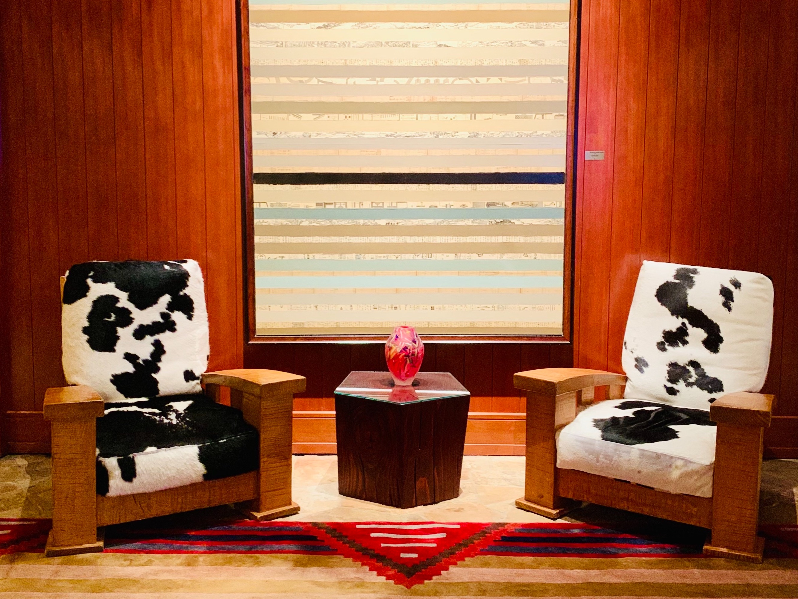 A stylish seating arrangement with black and white chairs, a red vase on a small table, and wooden paneling in the background.