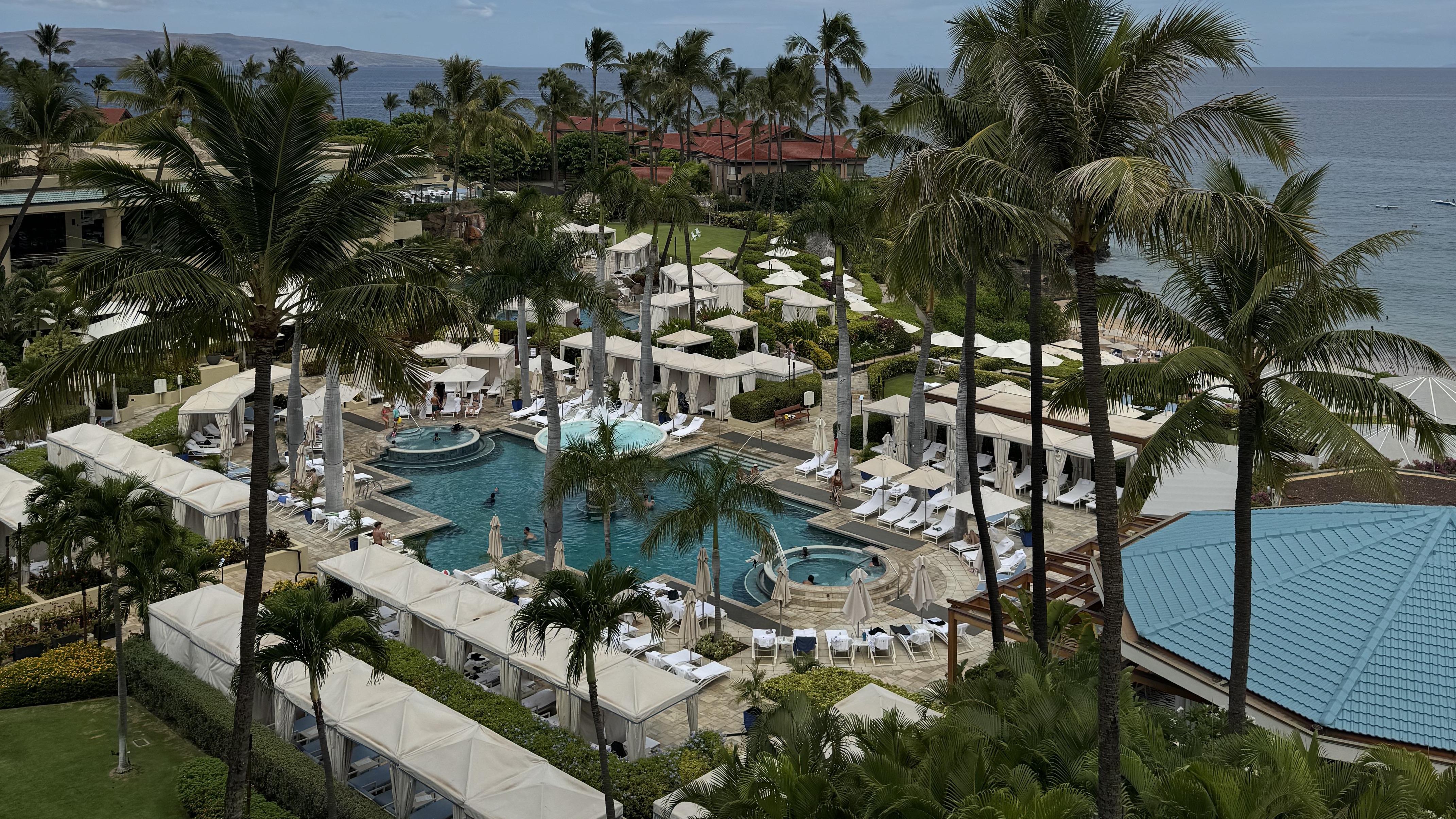 Hotel complex with buildings arranged around a pool and lots of palm trees.