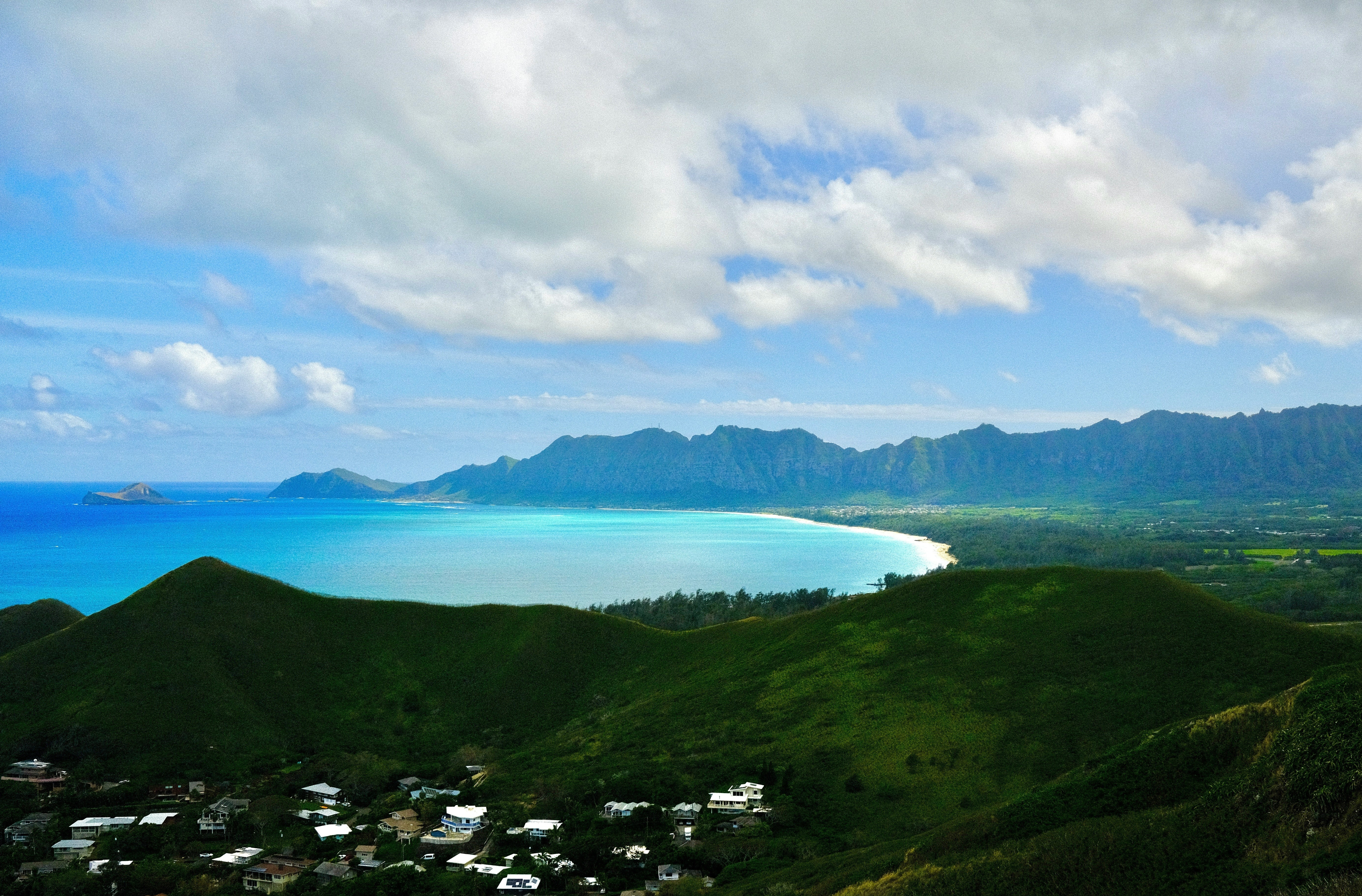 A scenic coastal landscape with lush greenery and mountains under a partly cloudy sky.