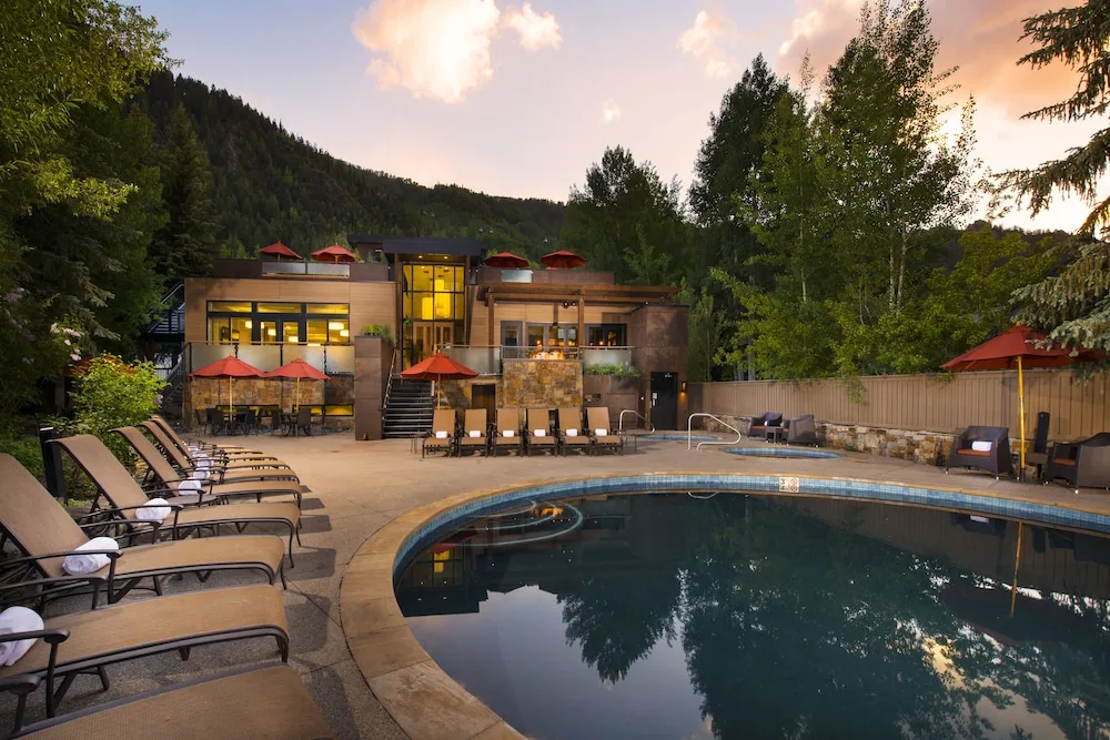 Loungers surround a pool and hot tub area. In the background, a contemporary structure offers refuge and forest surrounds the property