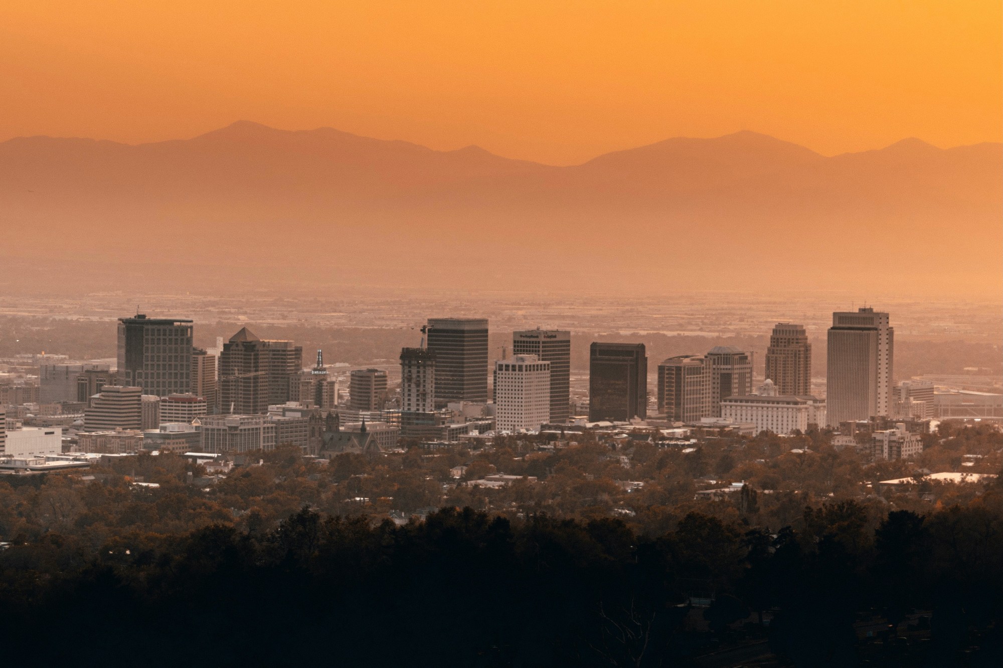 Skyline of city with buildings, mountains and a hazy orange sky.