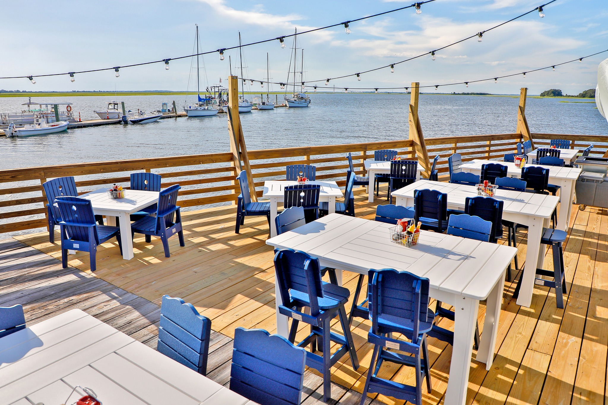 Blue chairs at white tables on a wooden deck over a body of water