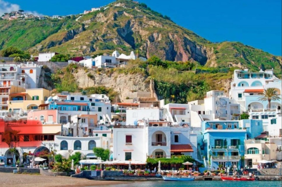 A coastal village with a grass-covered mountain in the distance