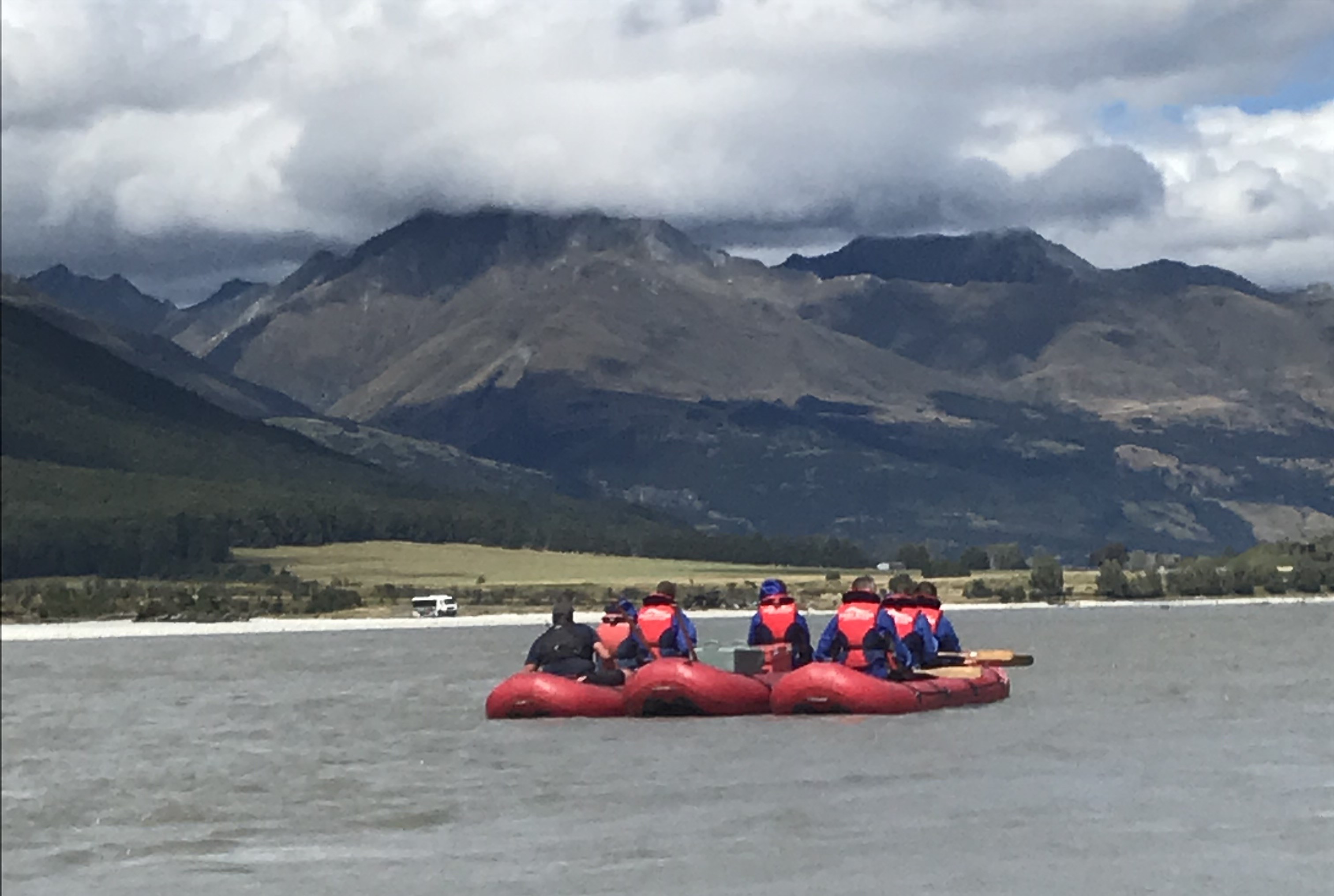 People in red kayaks against a backdrop of mountains on a cloudy day.