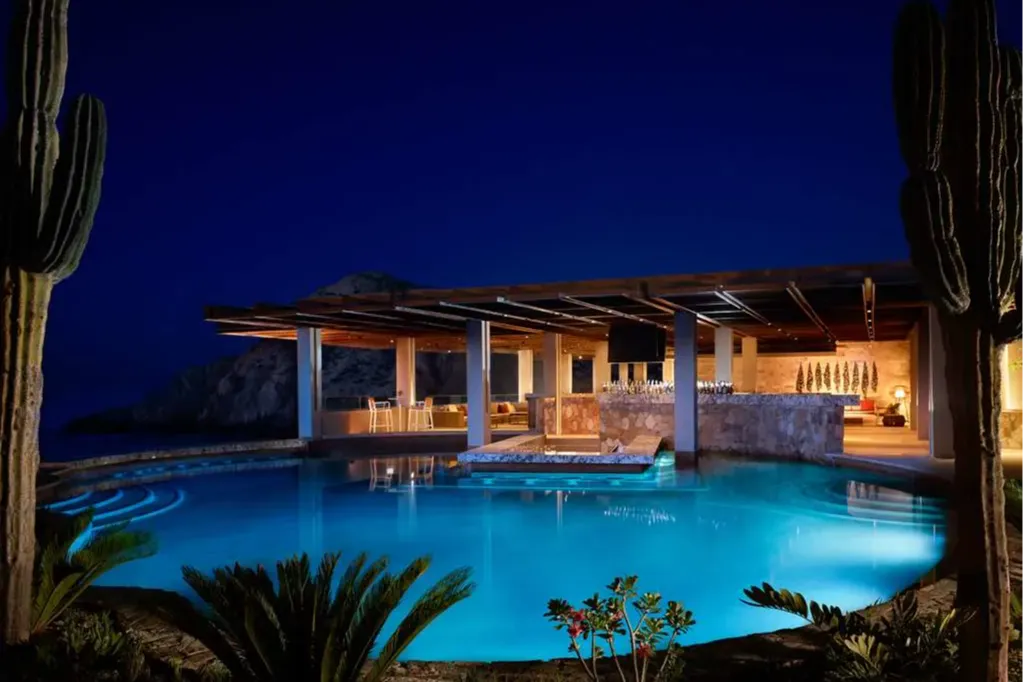 At night: a garden frames the photo. A well-lit pool leads up to an adjacent bar