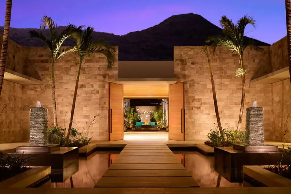 A footbridge crosses a small artificial water feature to a sleek stone entrance at Montage Los Cabos