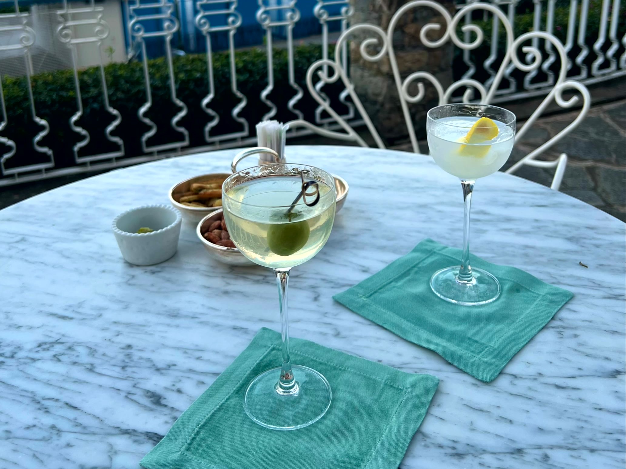 Two glasses of white wine with lemon slices and a bowl of olives on a table overlooking a serene sunset by the sea.