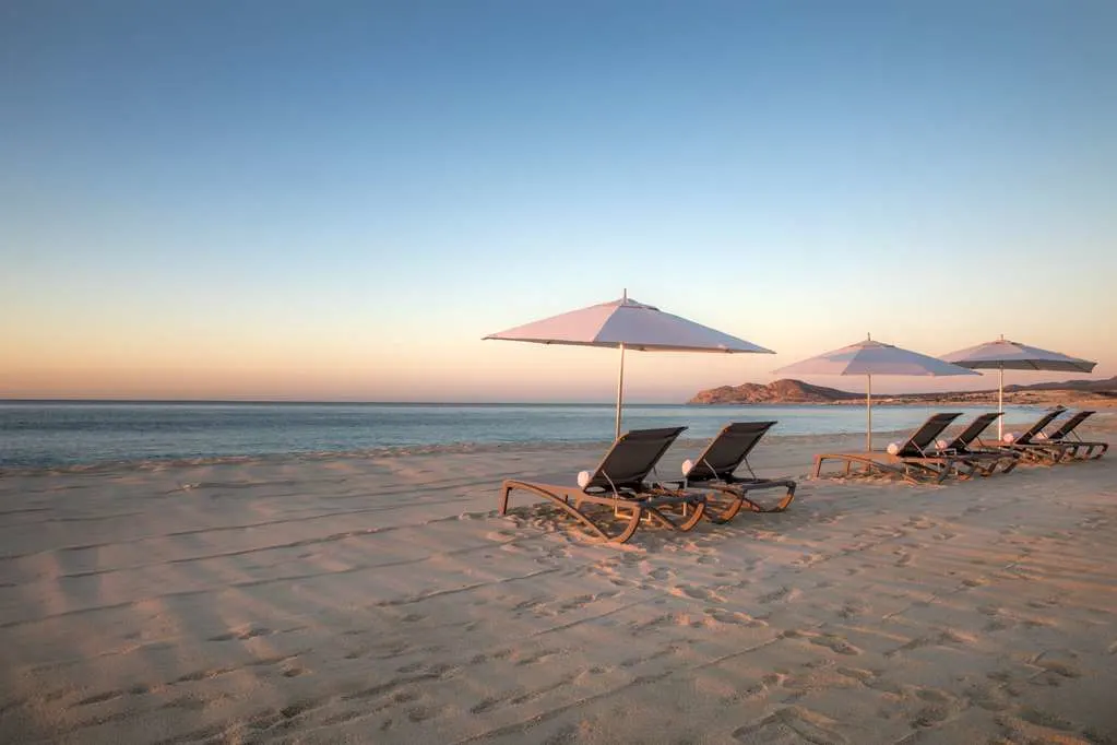 A couple loungers sit under an umbrella a pleasant looking beach at sunset