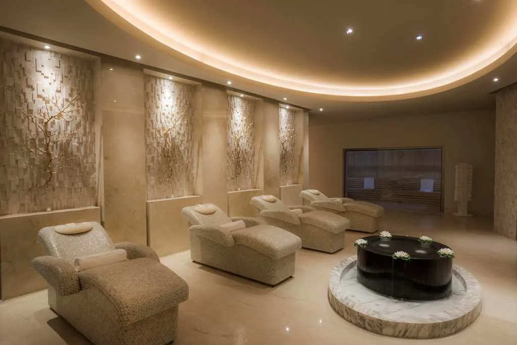 Four spa loungers in a tranquil looking room with a prominent water feature and pleasant lighting