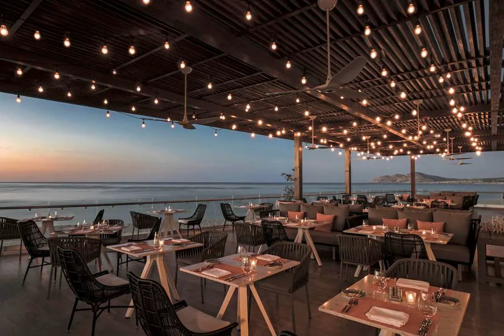 Contemporary cafe seating beneath a lengthy awning, with uninterrupted views of Loc Cabos' coast