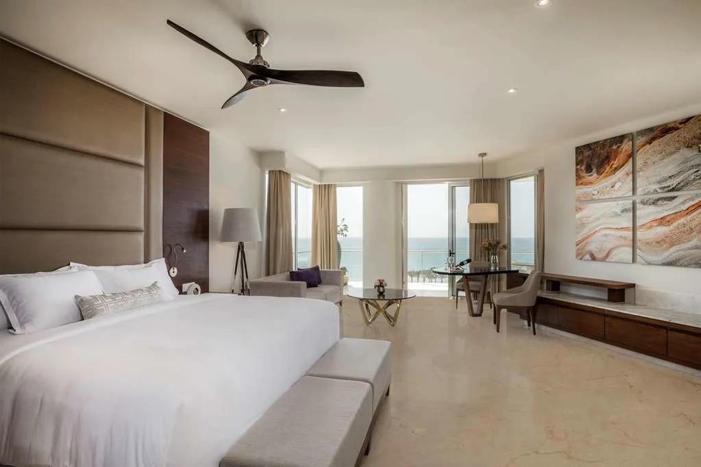 A spacious suite with a plush king bed, abstract art on the opposing wall, and a great view of the ocean from a balcony