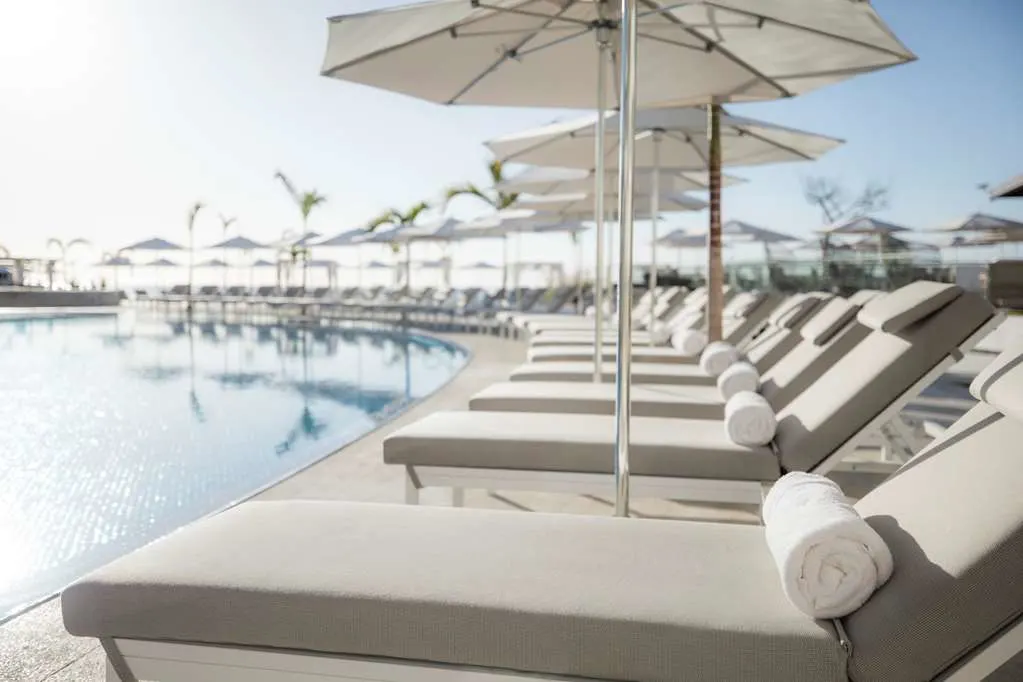 A row of contemporary loungers under umbrellas and next to an infinity pool