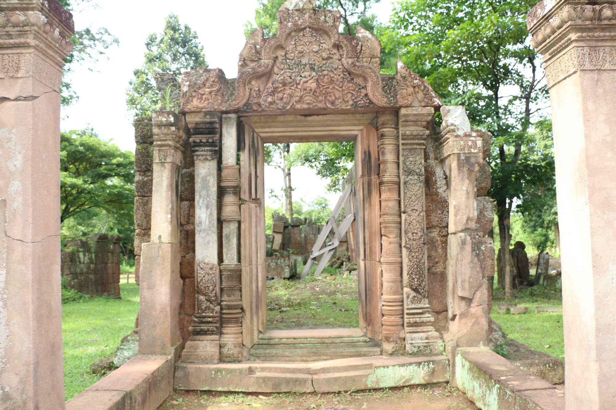 Cambodian ruins stand tall against the sky surrounded by lush trees and greenery.