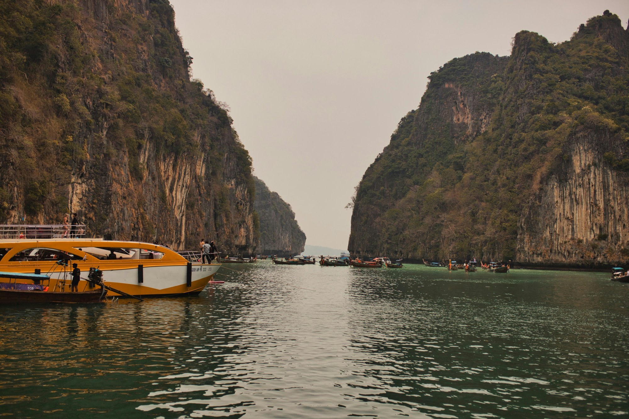 A speedboat floats in still waters as the waves gently lap near islands covered in lush greenery on a cloudy day.