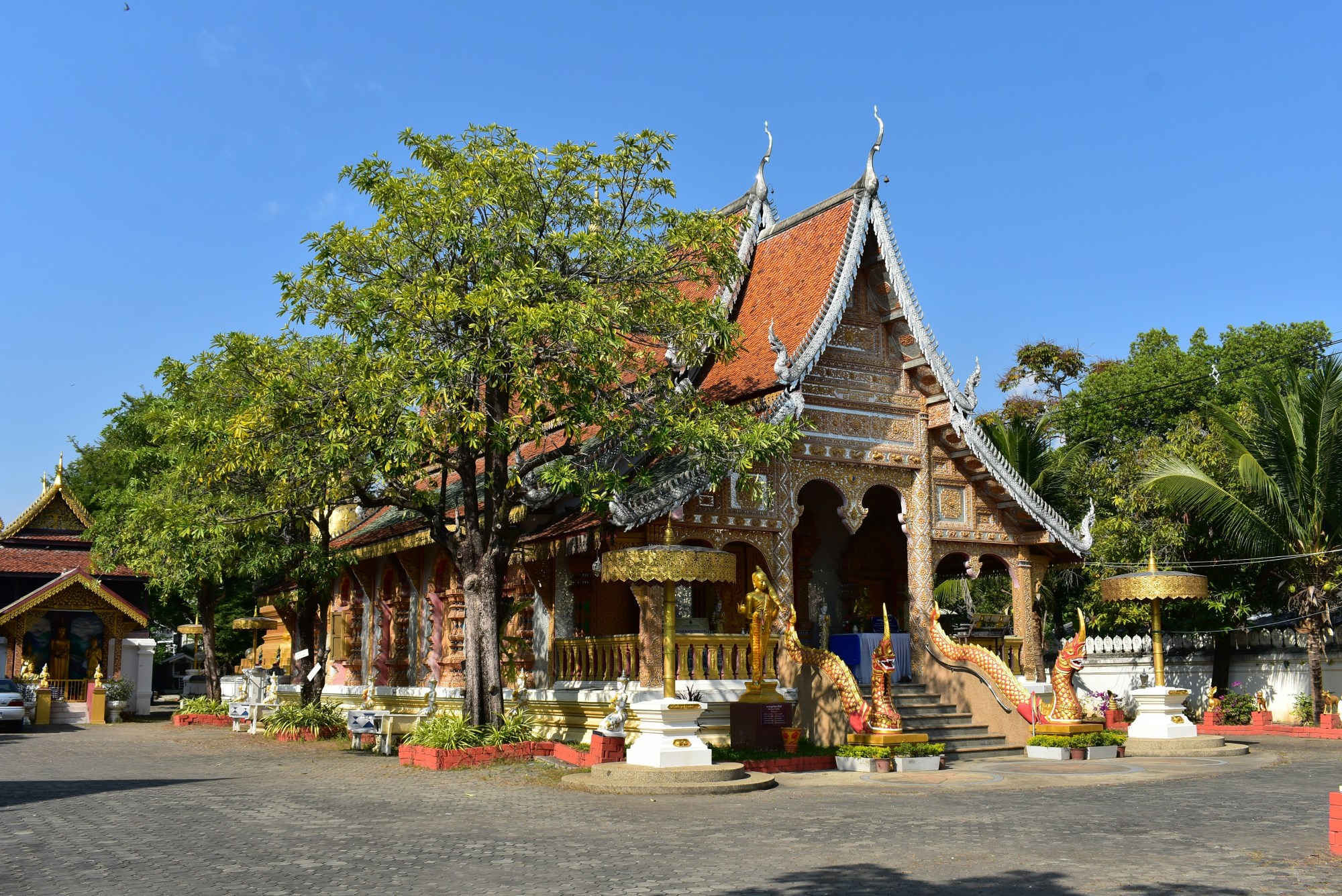 A Thai temple stands against the sky on a clear day under lush trees.