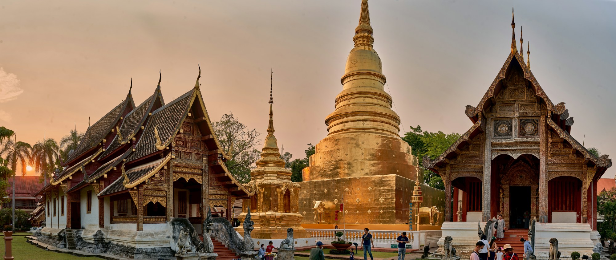 Buddhist temples reach toward the sky at sunset as visitors mill below.