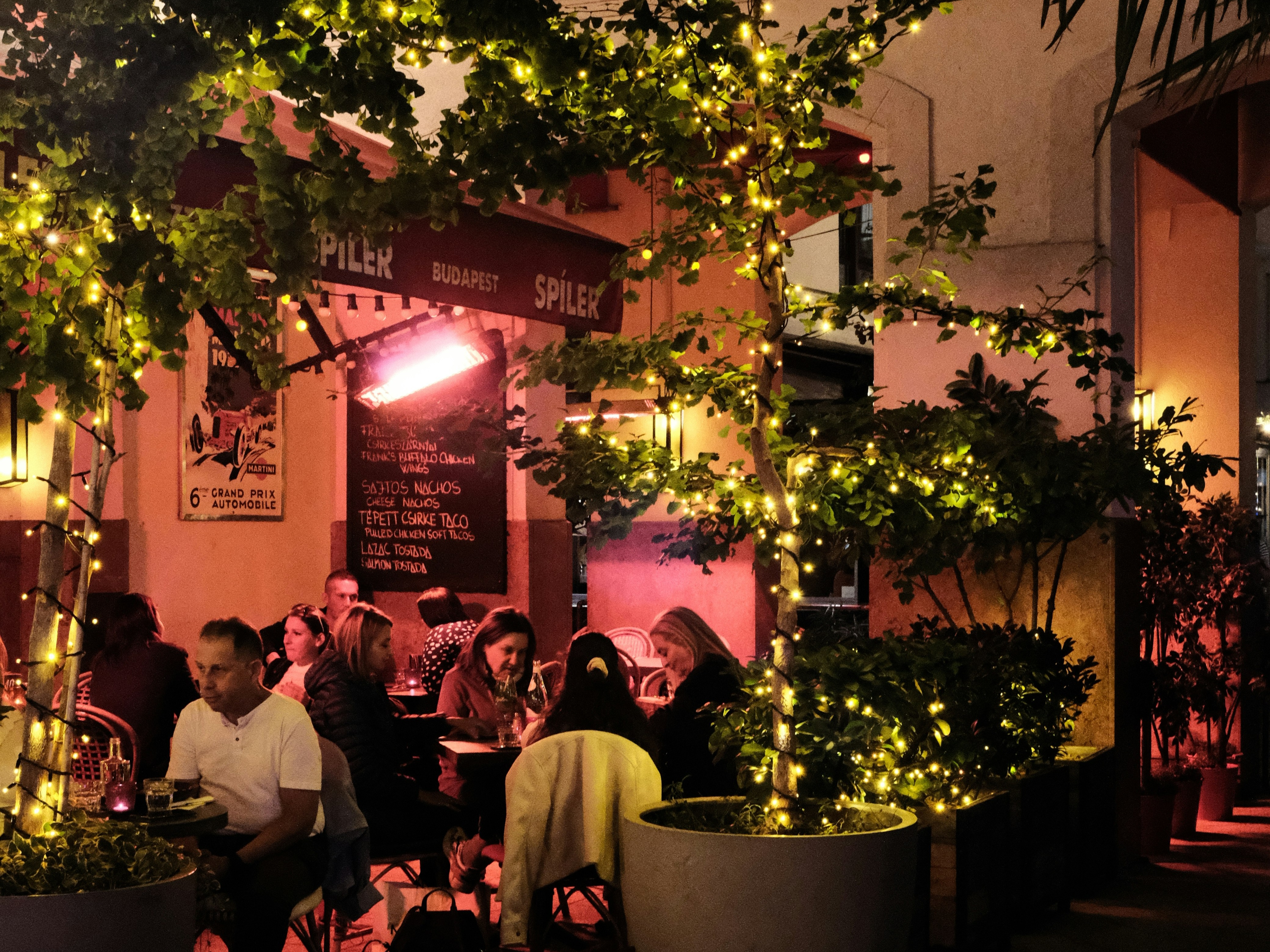 An outdoor dining area at night, warmly lit with patrons enjoying their meals.