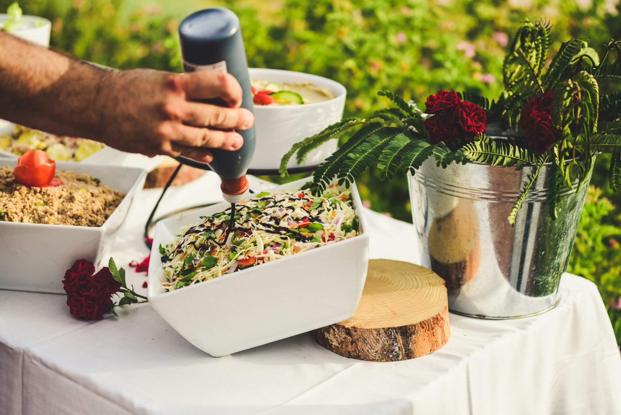A person's hand putting dressing a salad on a full banquet table with flowers.