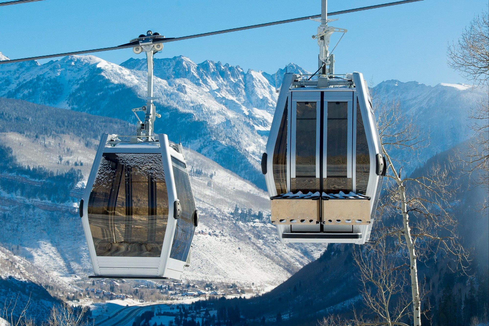 Twin cable cars ascend up the slopes of Vail Ski Resort with snowy mountains in the background