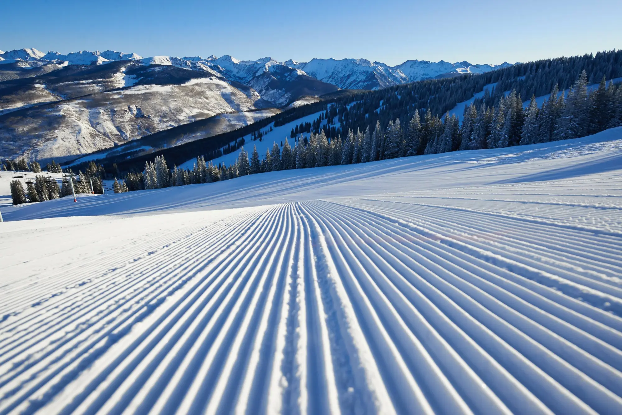 Well-manicured ski slopes lined by snowy pine trees and snowcapped mountains in the distance