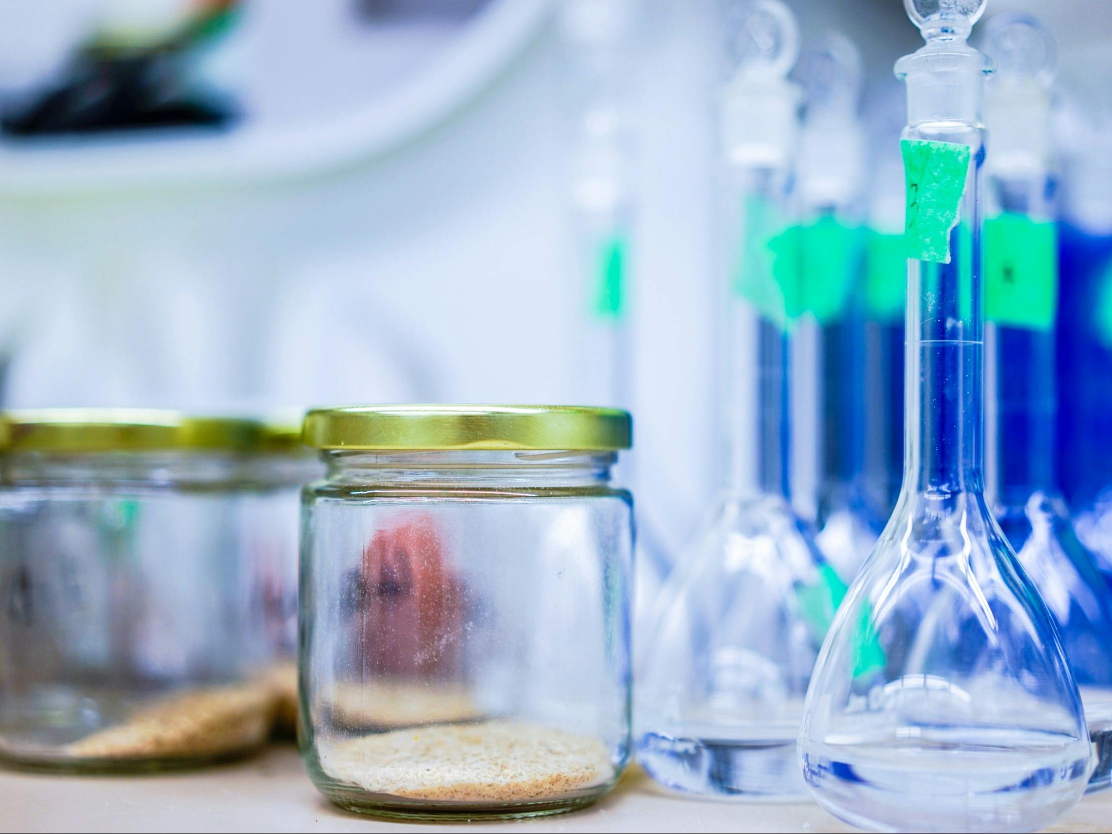 Laboratory glassware containing blue liquid is arranged on a blurred background, highlighting scientific research or chemical analysis.