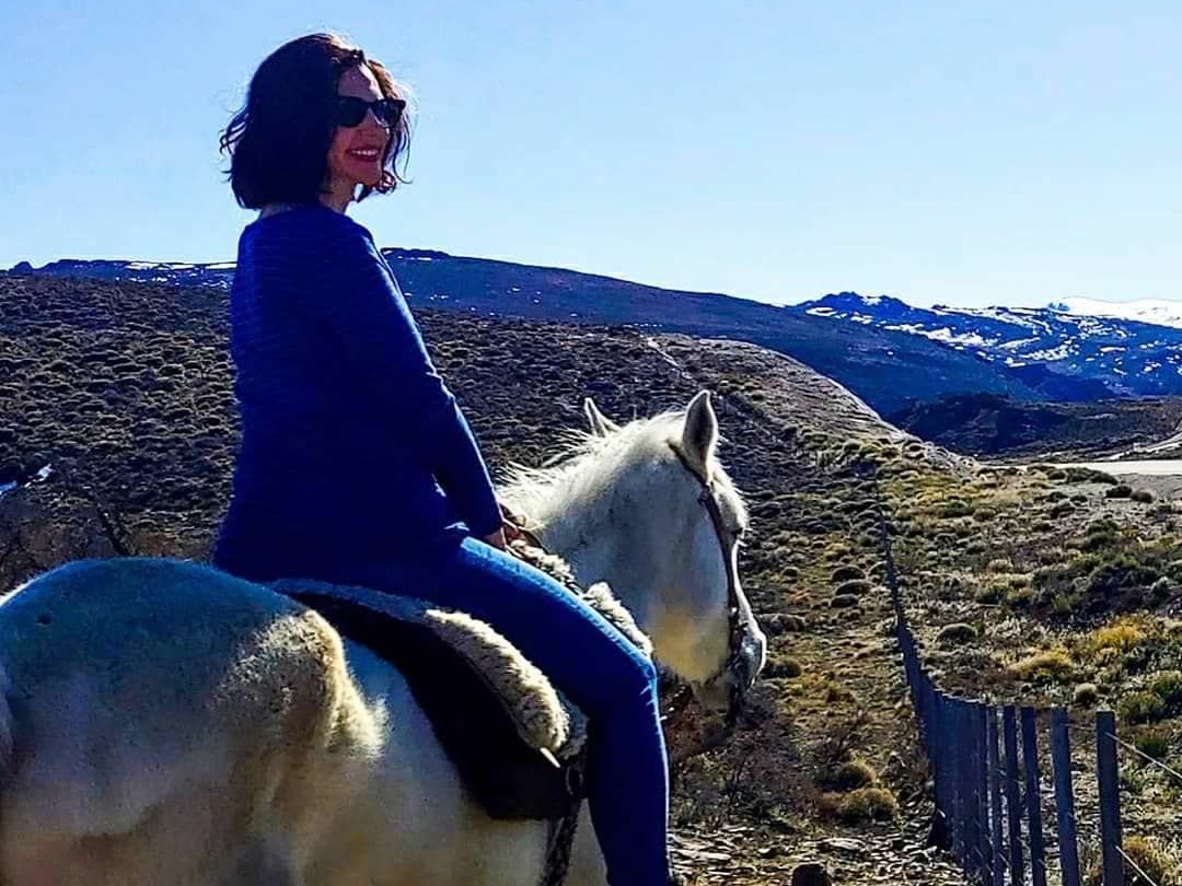A pixelated-faced individual is riding a white horse in a hilly, outdoor setting with sparse vegetation and a clear sky.