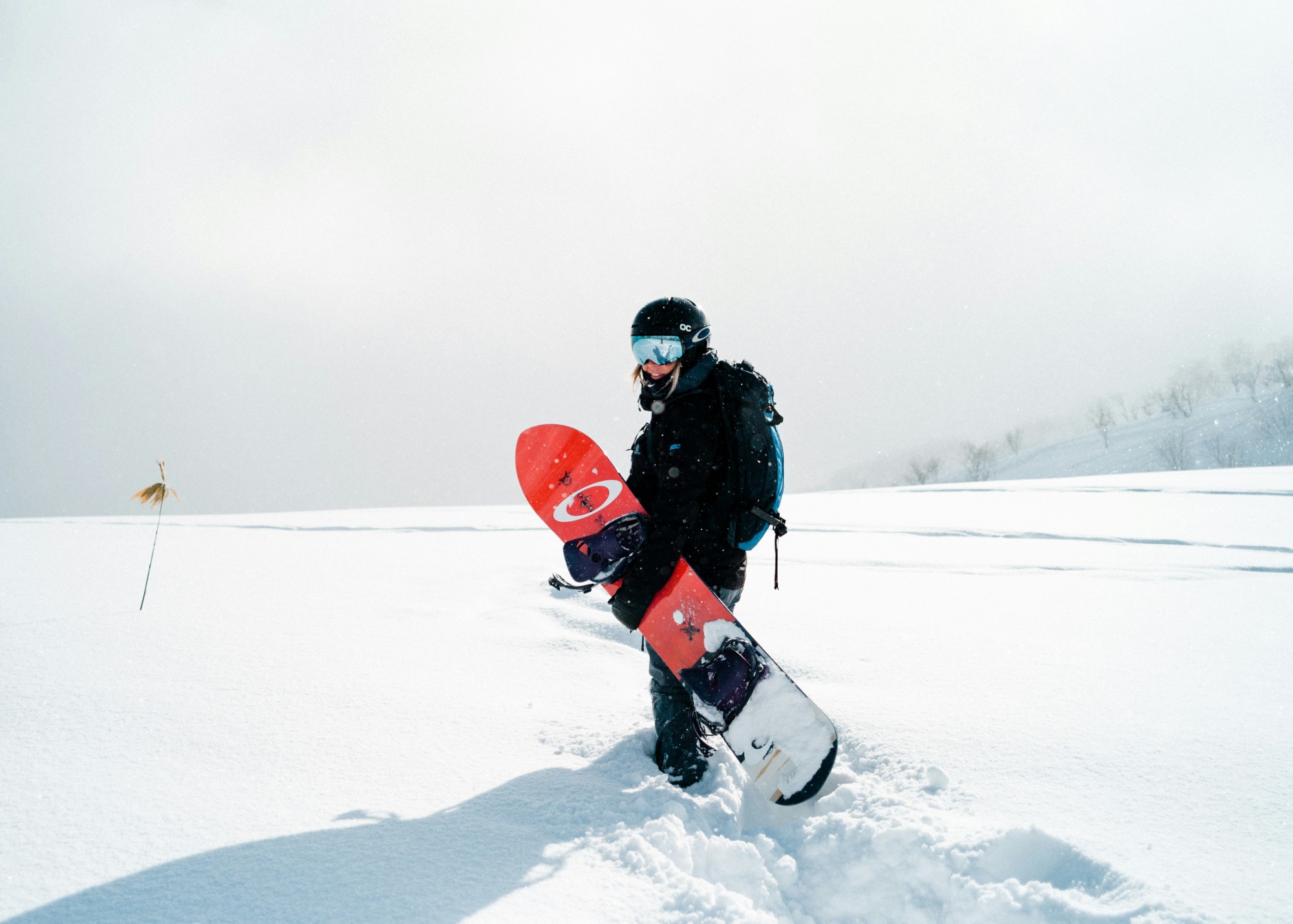 A man holding a red snowboard on a snowy field.