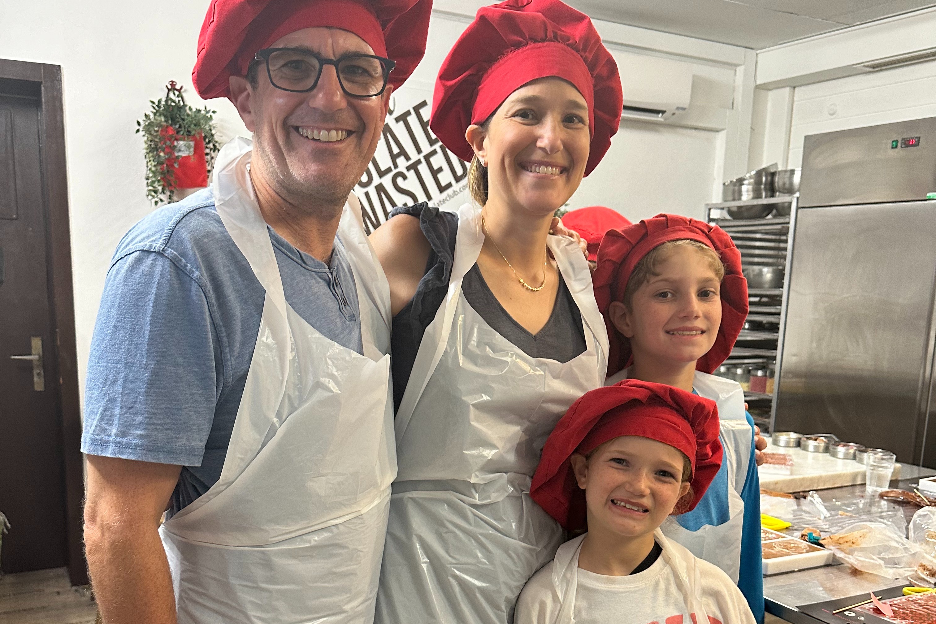 A family of four wearing white aprons and red chef hats.
