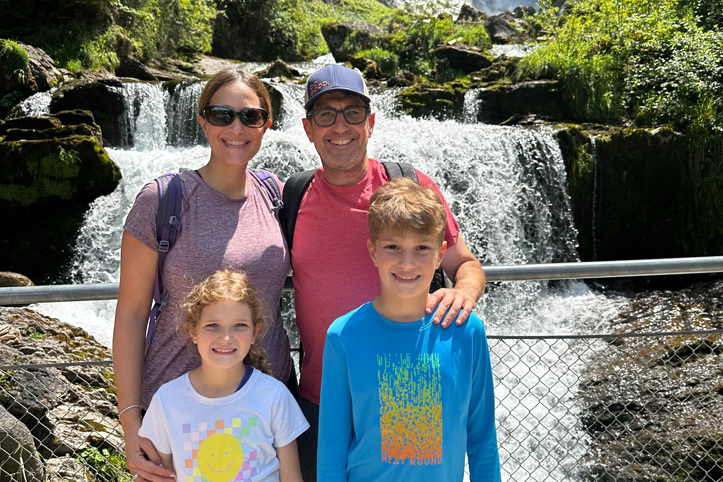 A family of four poses in front of a waterfall.