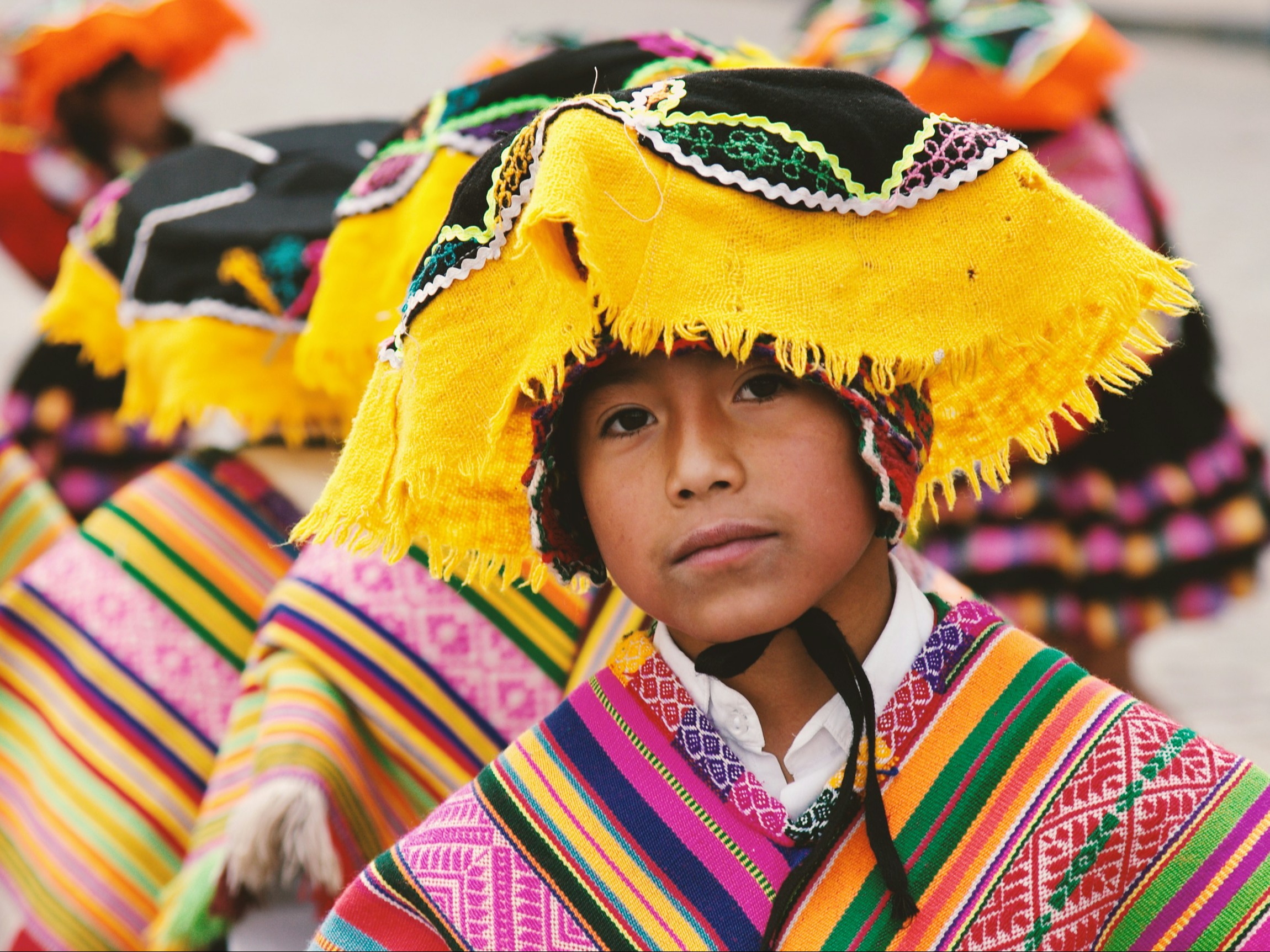 A group of individuals in colorful traditional attire is captured, with one person’s face obscured by a blurred rectangle.