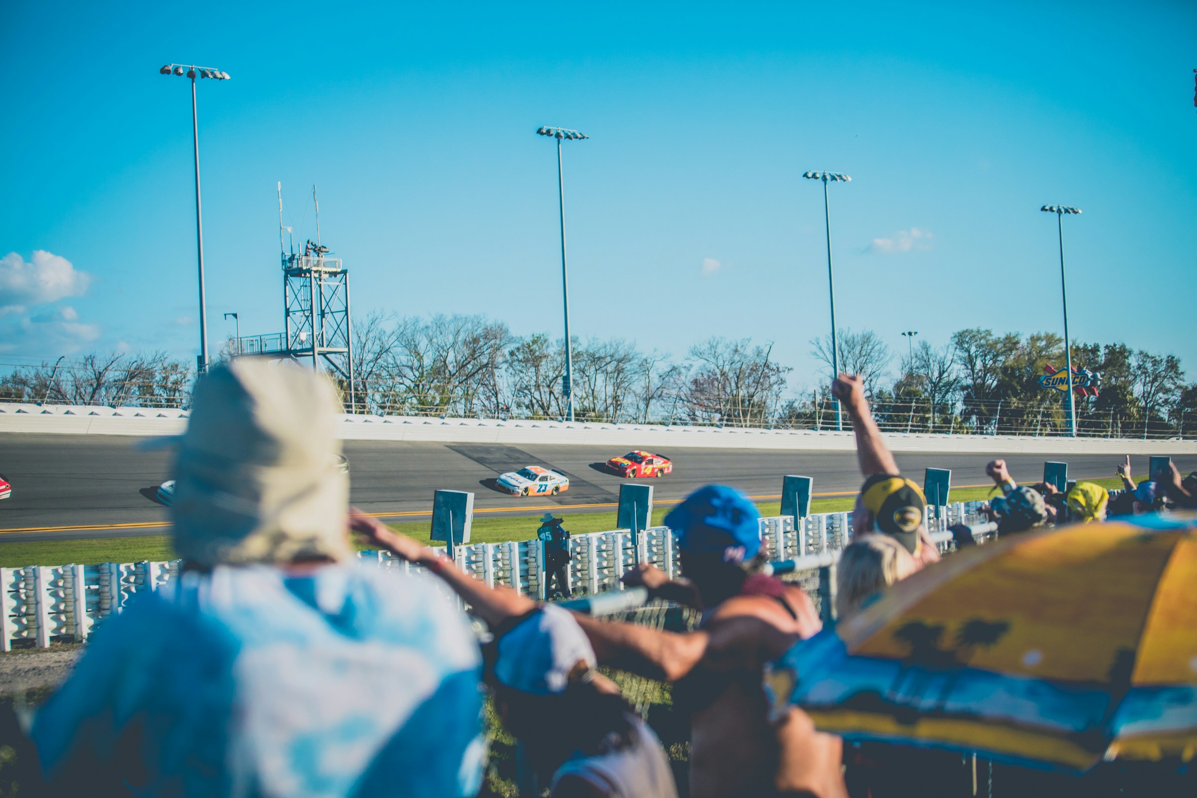 Spectators watching race cars on a banked race track.