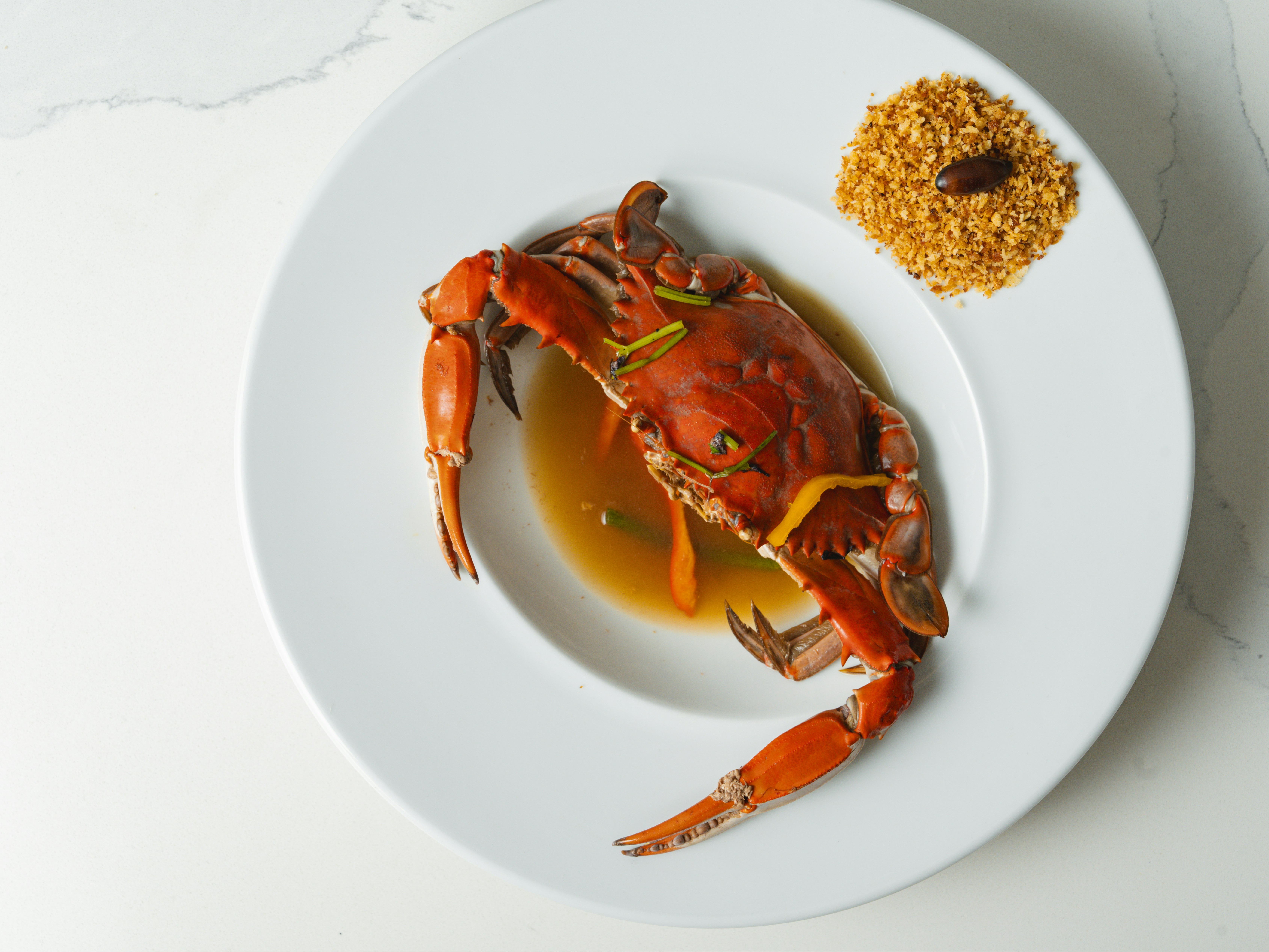 The image shows a cooked crab on a white plate with a side of seasoning.