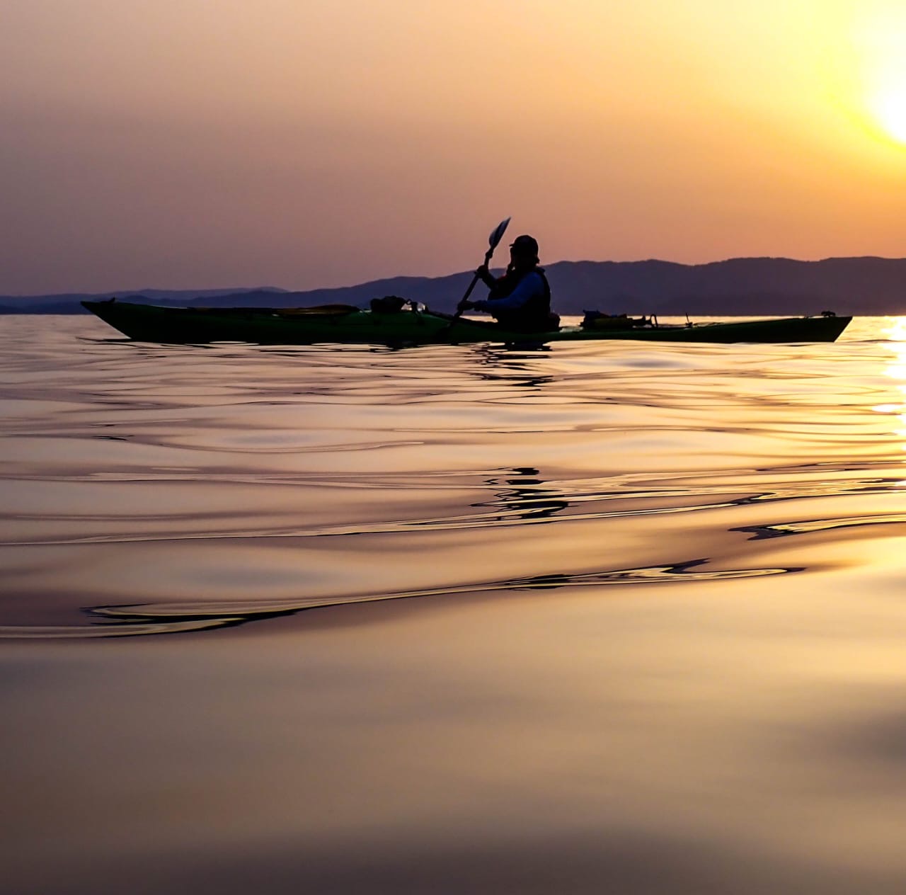 A person kayaking on the water during a sunset