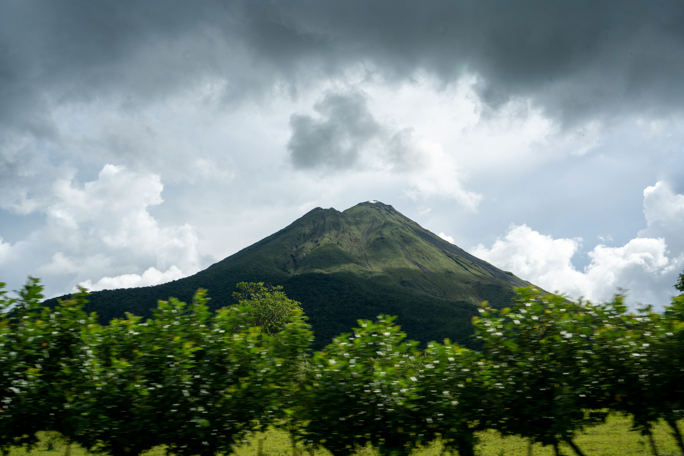 View of the Arenal Volcano surrounded by lush greenery on a cloudy day.