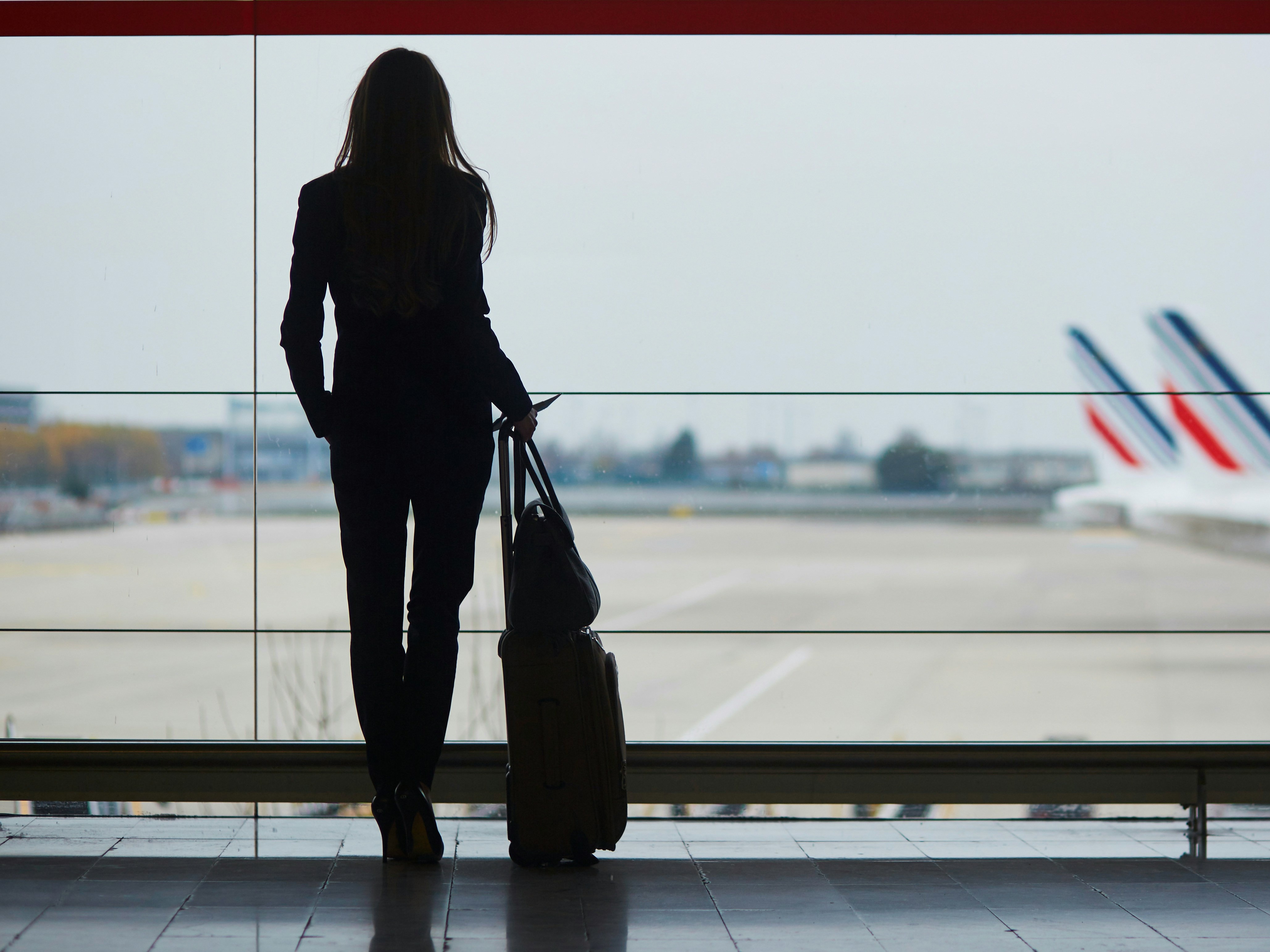 A silhouette of an individual standing in an airport terminal, looking out at airplanes on the tarmac.