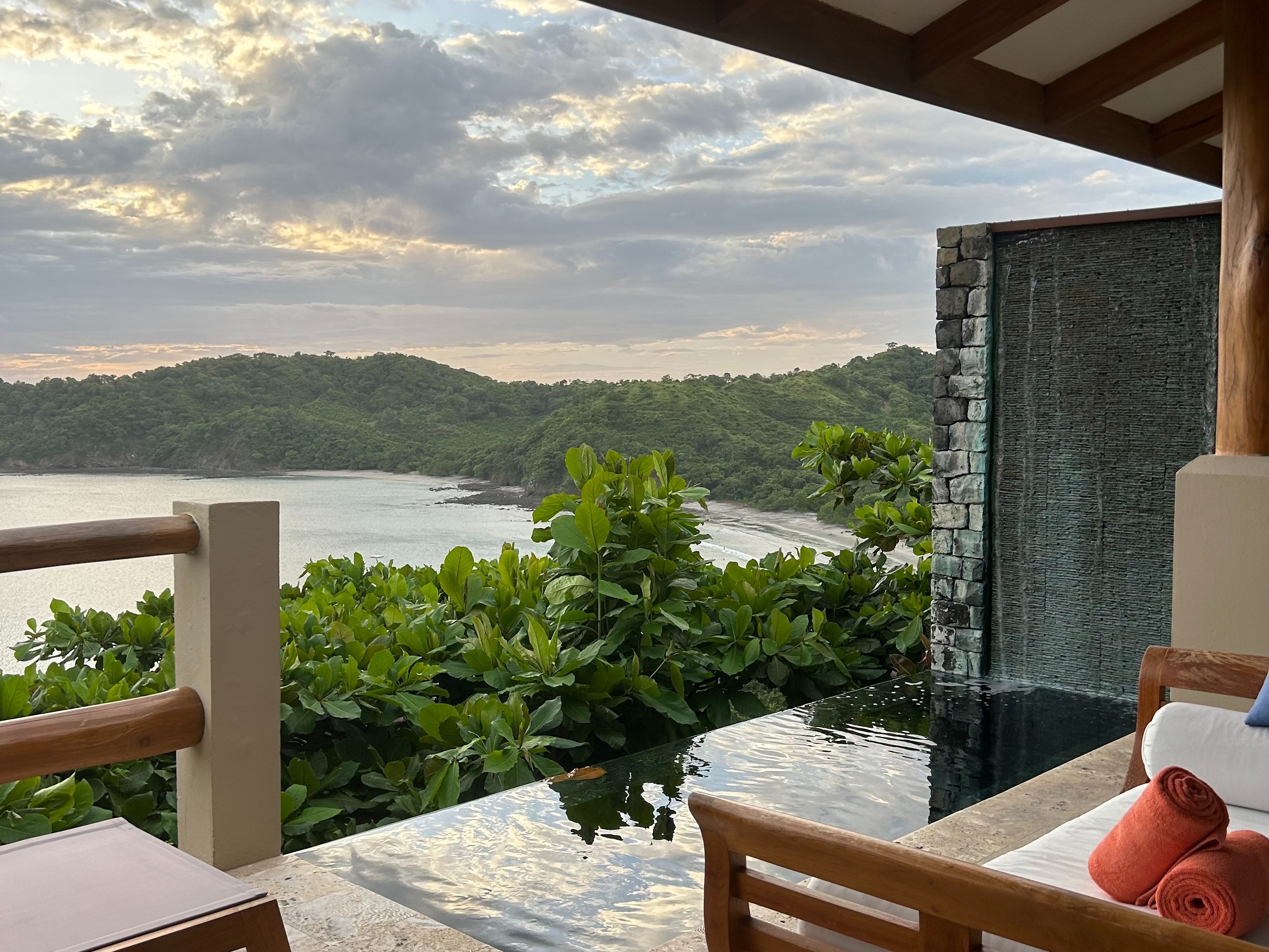 A scenic view from a balcony overlooking a lush green landscape and water body during sunset or sunrise.