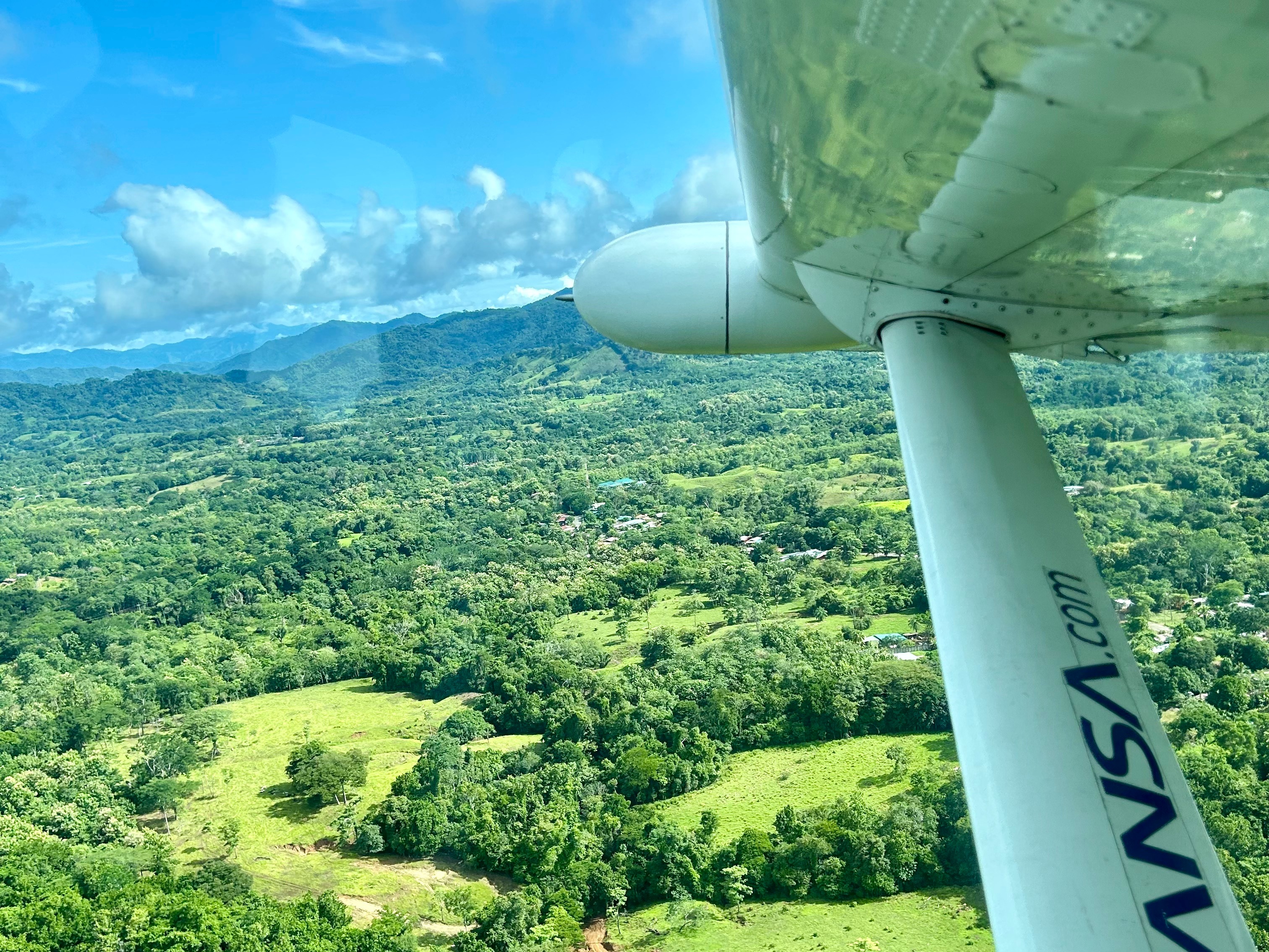 A view from an airplane window showing a lush green landscape with the airplane’s wing in the foreground.
