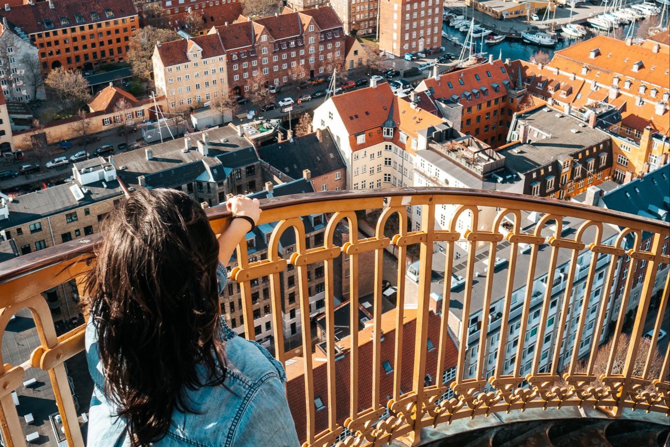 a woman stands near a yellow railing overlooking colorful rooftops