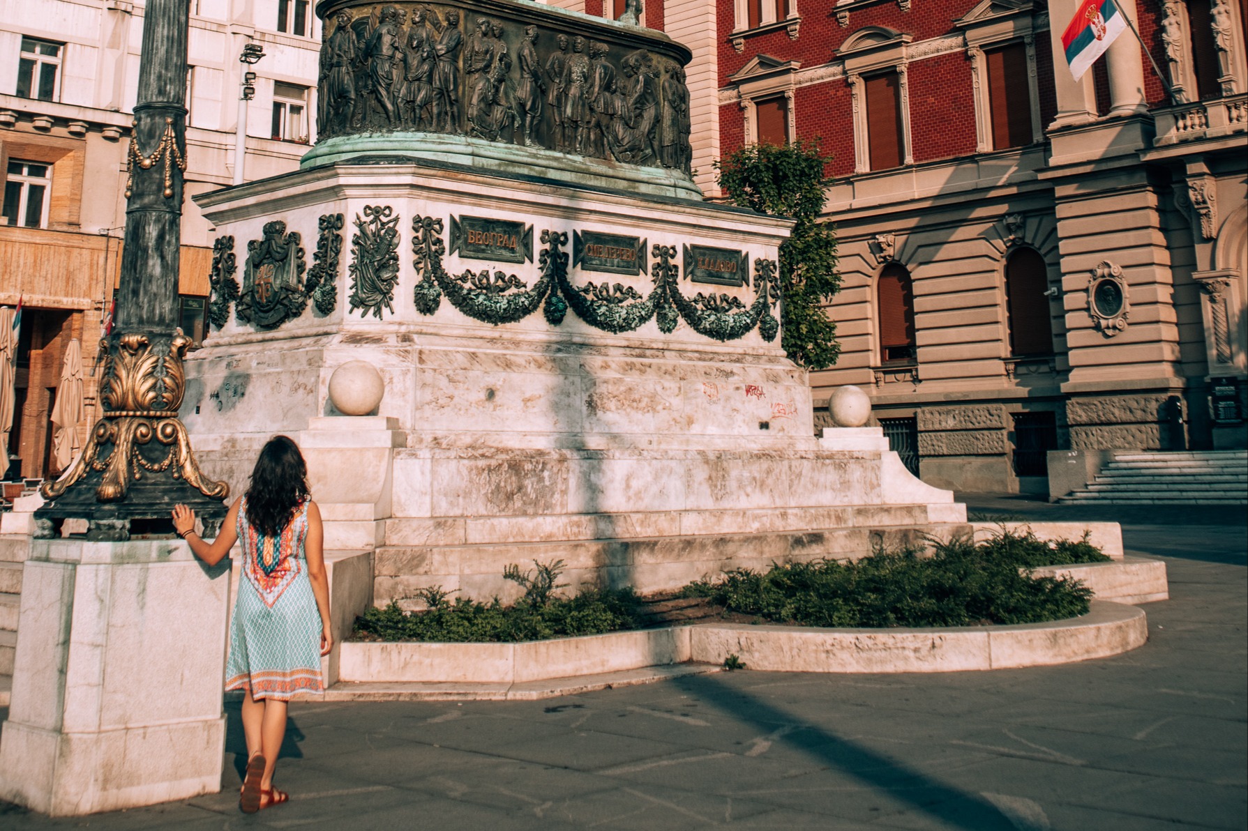 a woman stands near a lamp post in an old city square