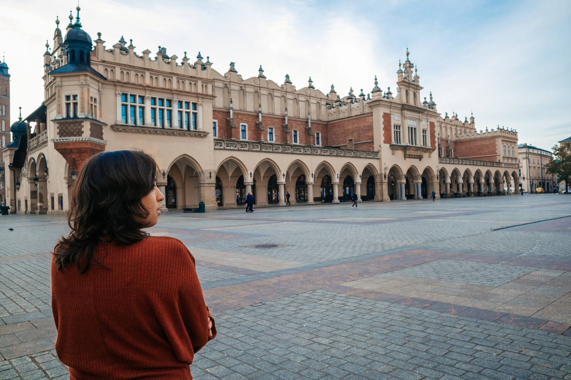 a woman in a red sweater stands in an old city square