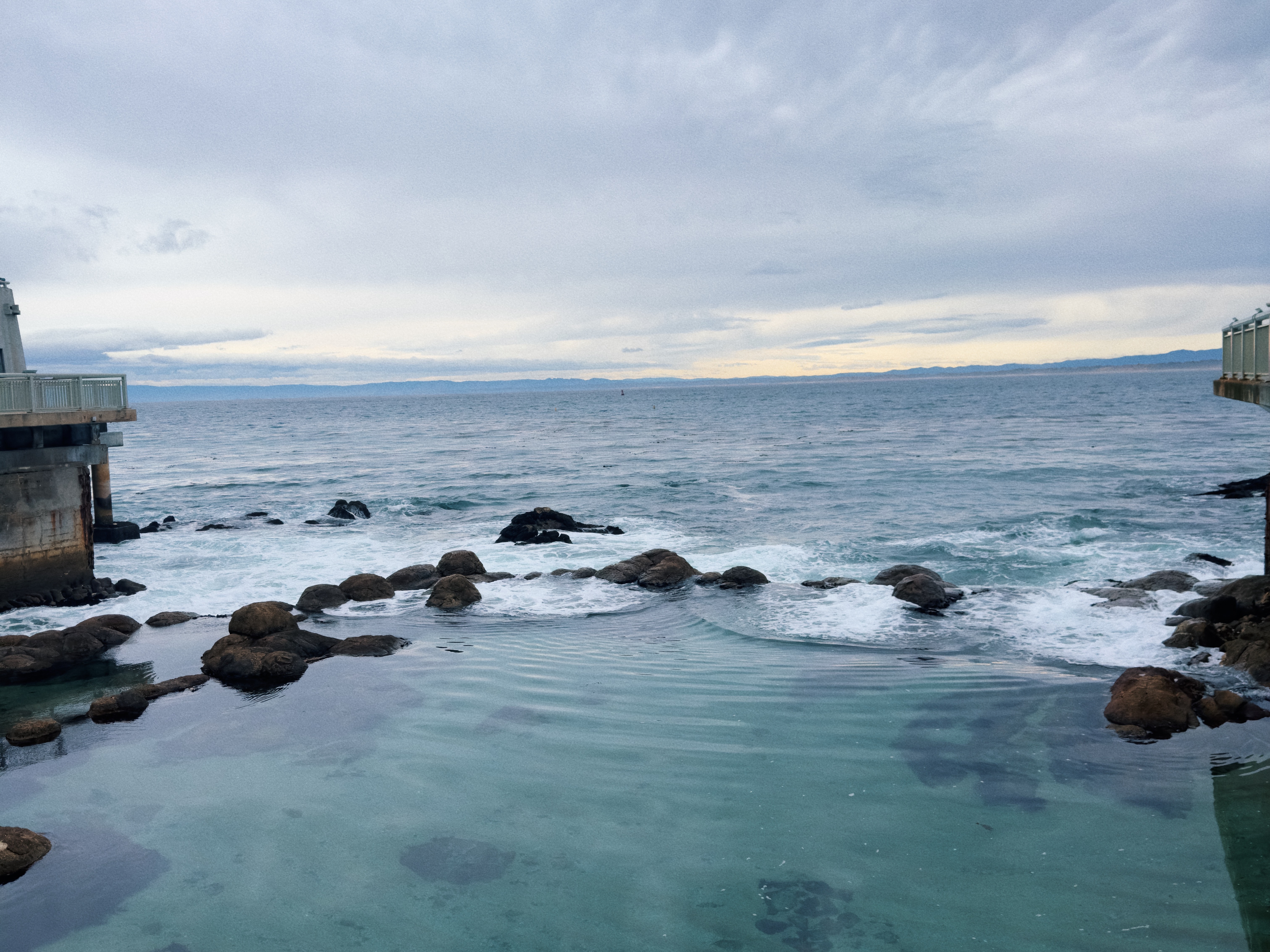 The image shows a tranquil seascape with clear waters in the foreground and a cloudy sky above.